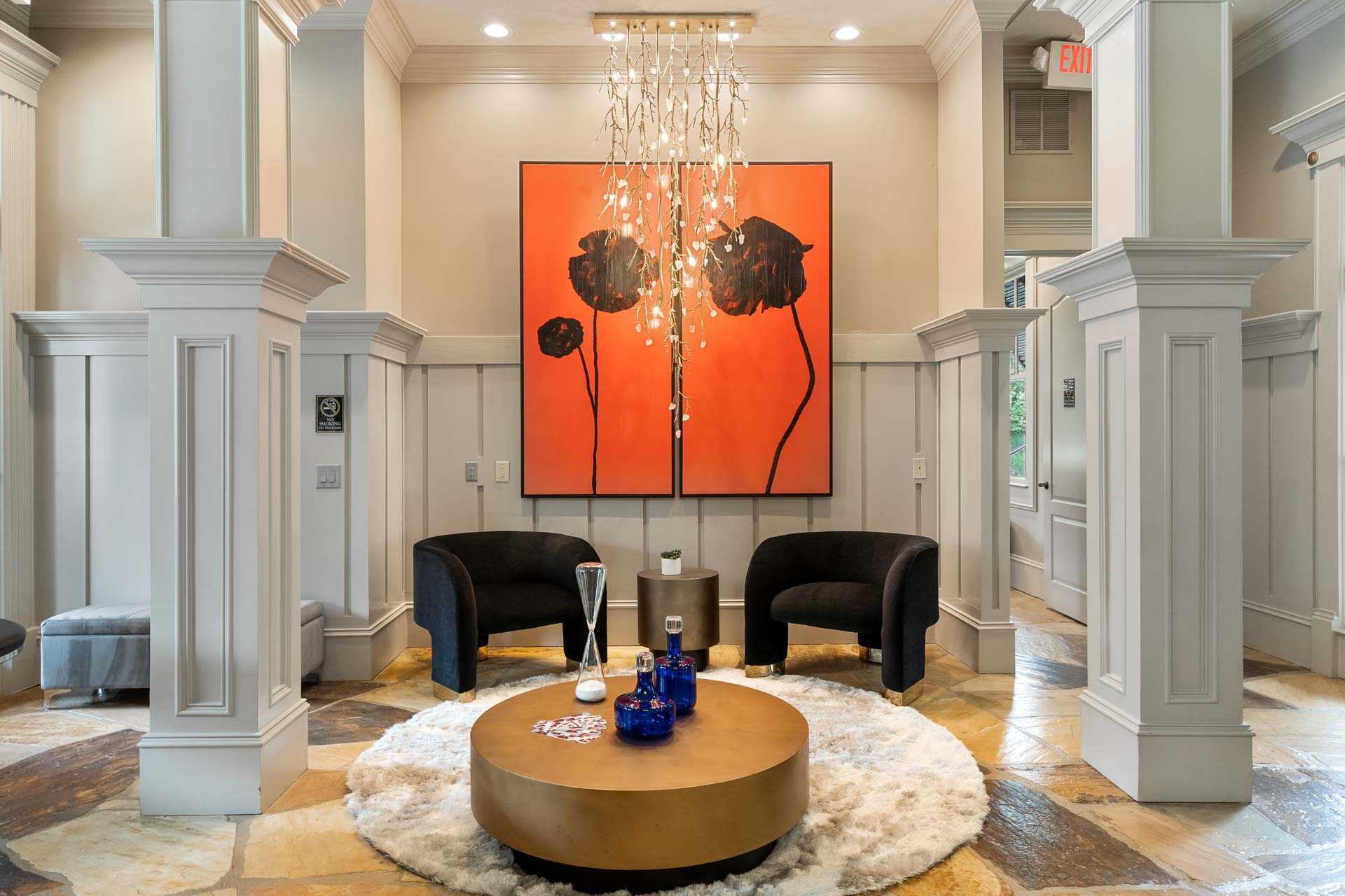 Elegant lounge at The Village at Towne Lake in Woodstock GA with abstract orange floral art, crystal chandelier, black armchairs, and gold coffee table