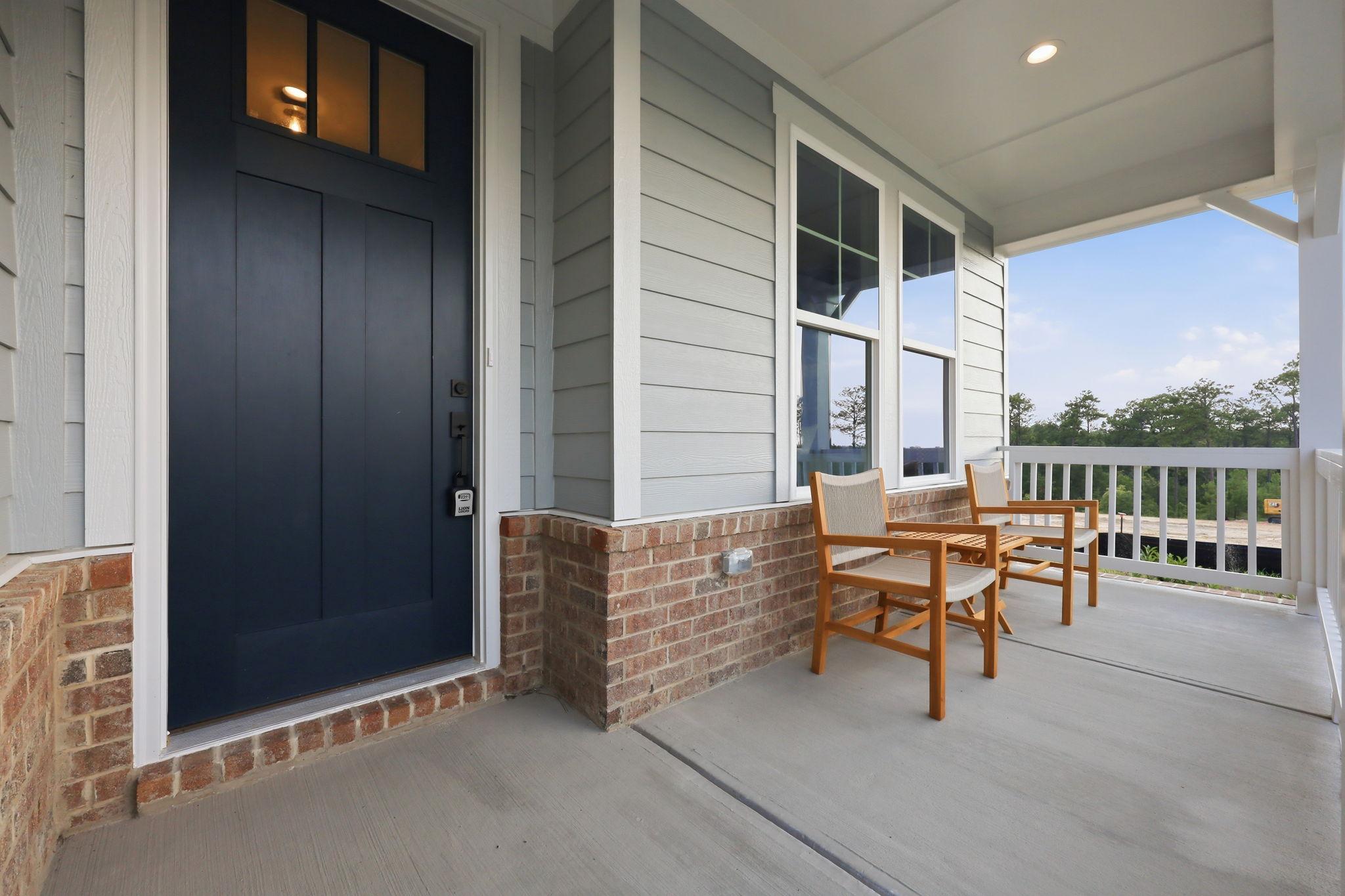 Covered front porch of The Beech B home design featuring brick and vinyl exterior with dark blue door in Holly Springs, NC.