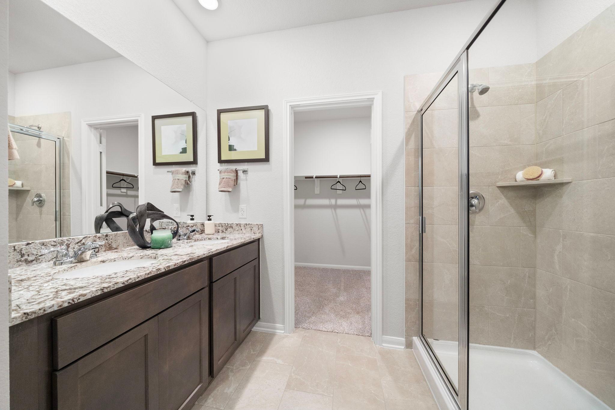 Spacious master bathroom at Caney Creek Place in Conroe TX with double dark vanity, granite counters, and glass walk-in shower