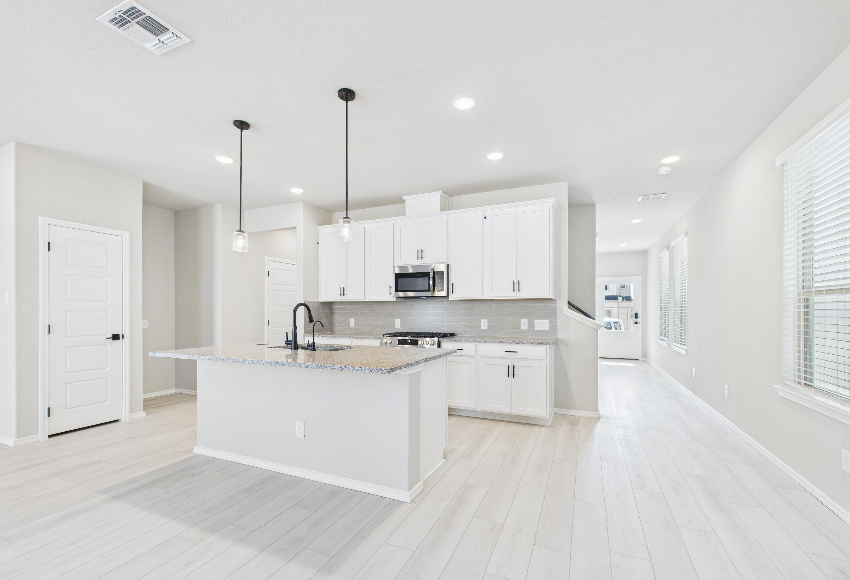 Modern open-concept kitchen in The Charlotte A featuring white cabinets, granite countertops, and pendant lighting.