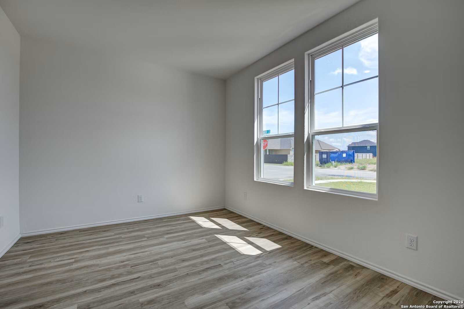 Bright empty bedroom with luxury vinyl plank flooring and large sunny windows in Davidson Homes The Douglas B, Seguin, Texas