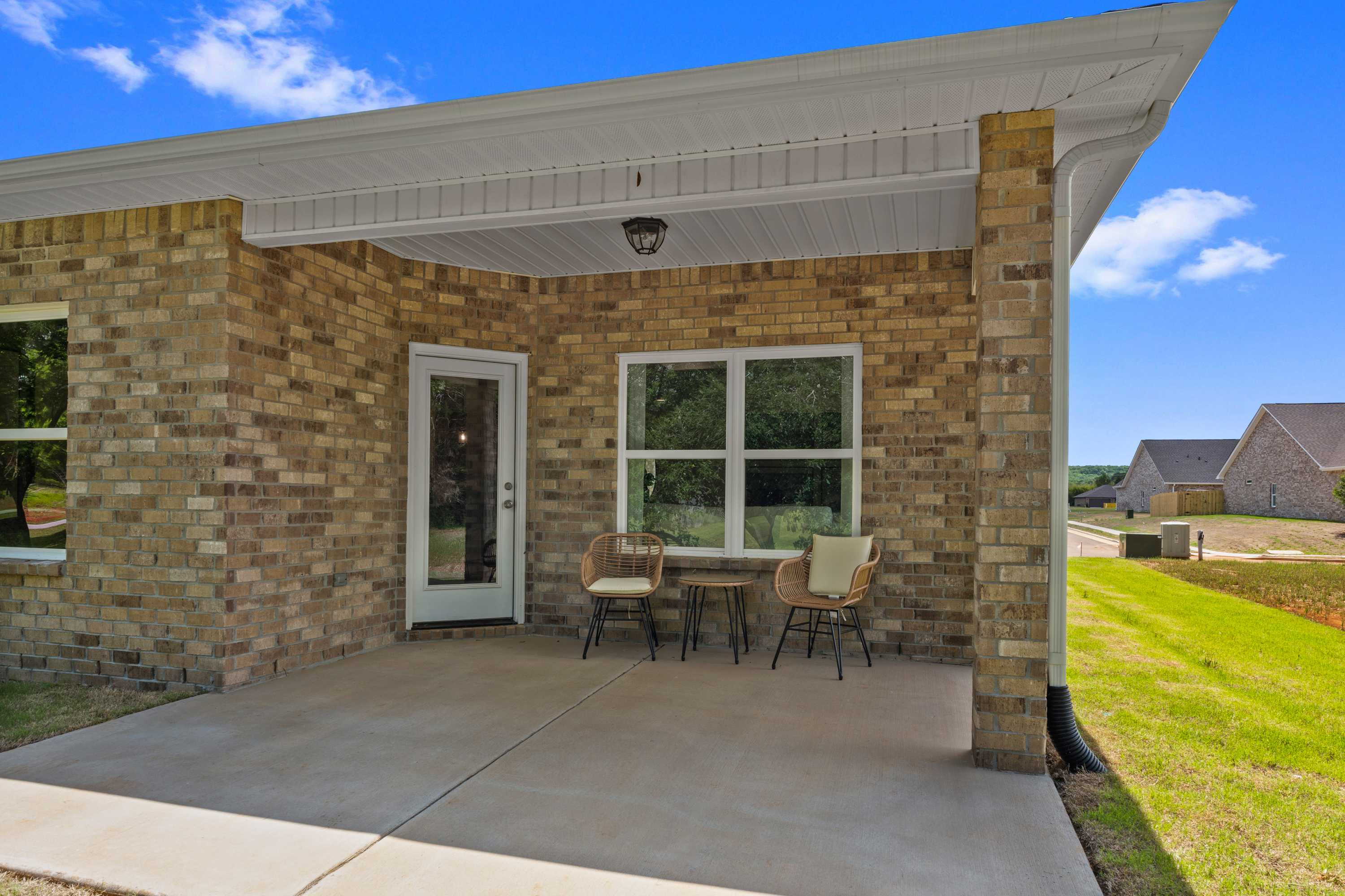 Brick home covered porch at Hollon Meadow in Decatur Alabama with wicker seating green lawn and blue sky
