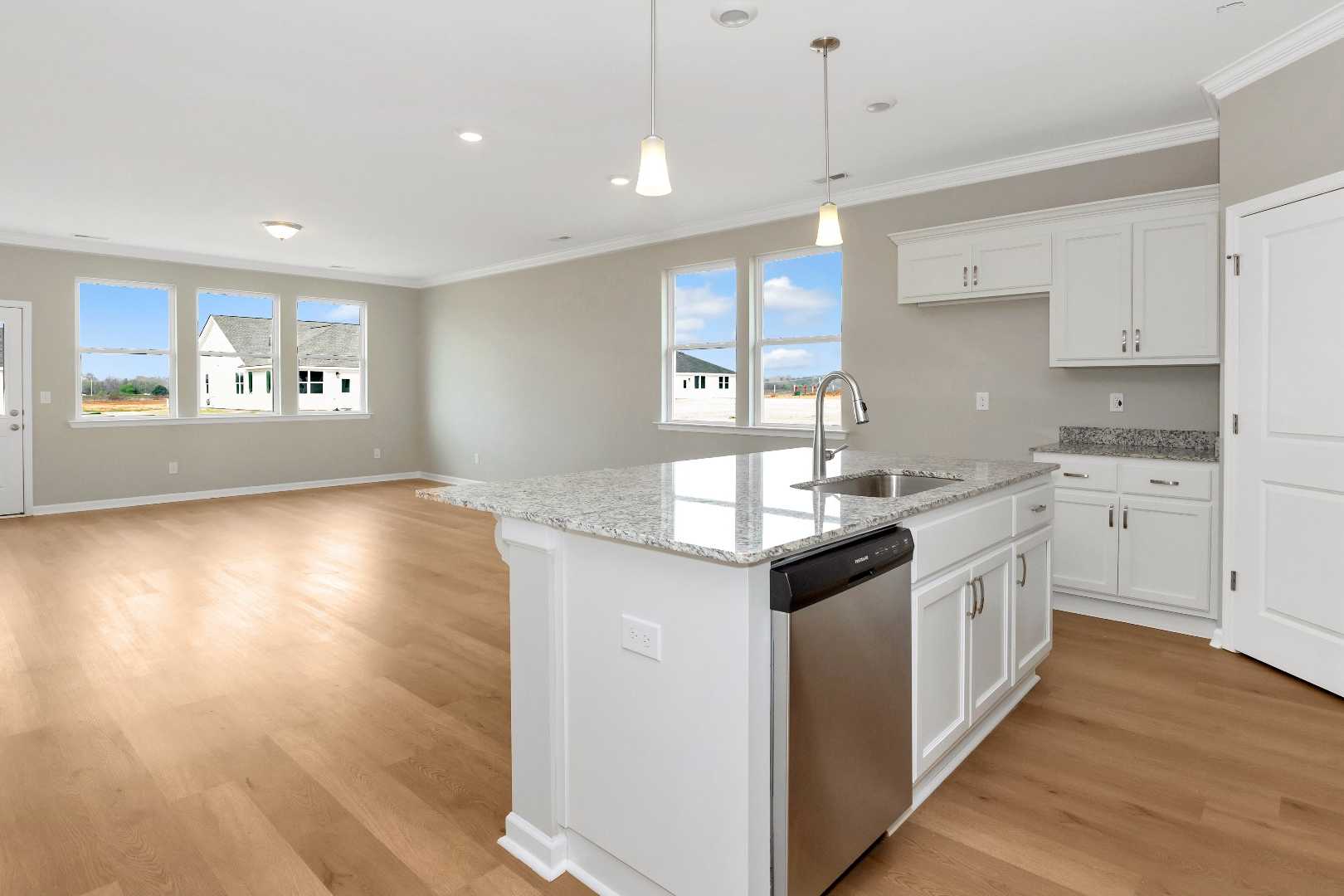 Spacious open-concept kitchen in The Orion featuring white shaker cabinets, granite island sink, and hardwood floors