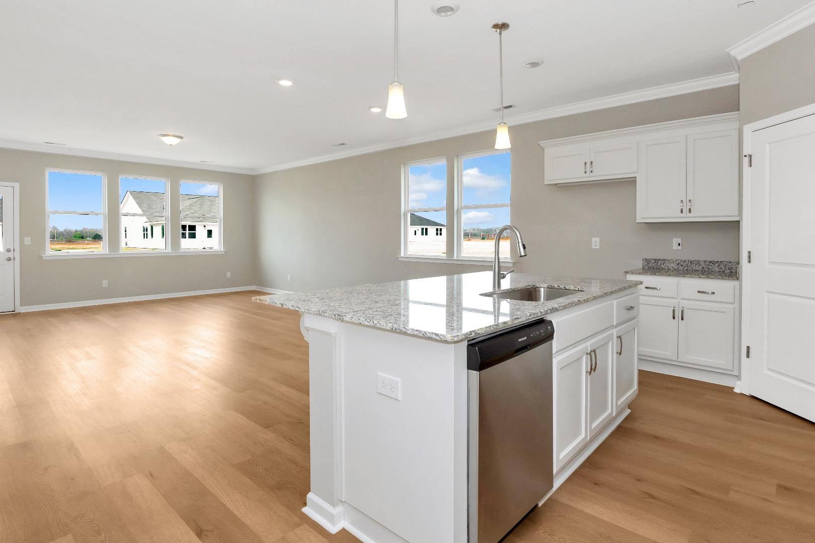 Spacious open-concept kitchen in The Orion featuring white shaker cabinets, granite island sink, and hardwood floors