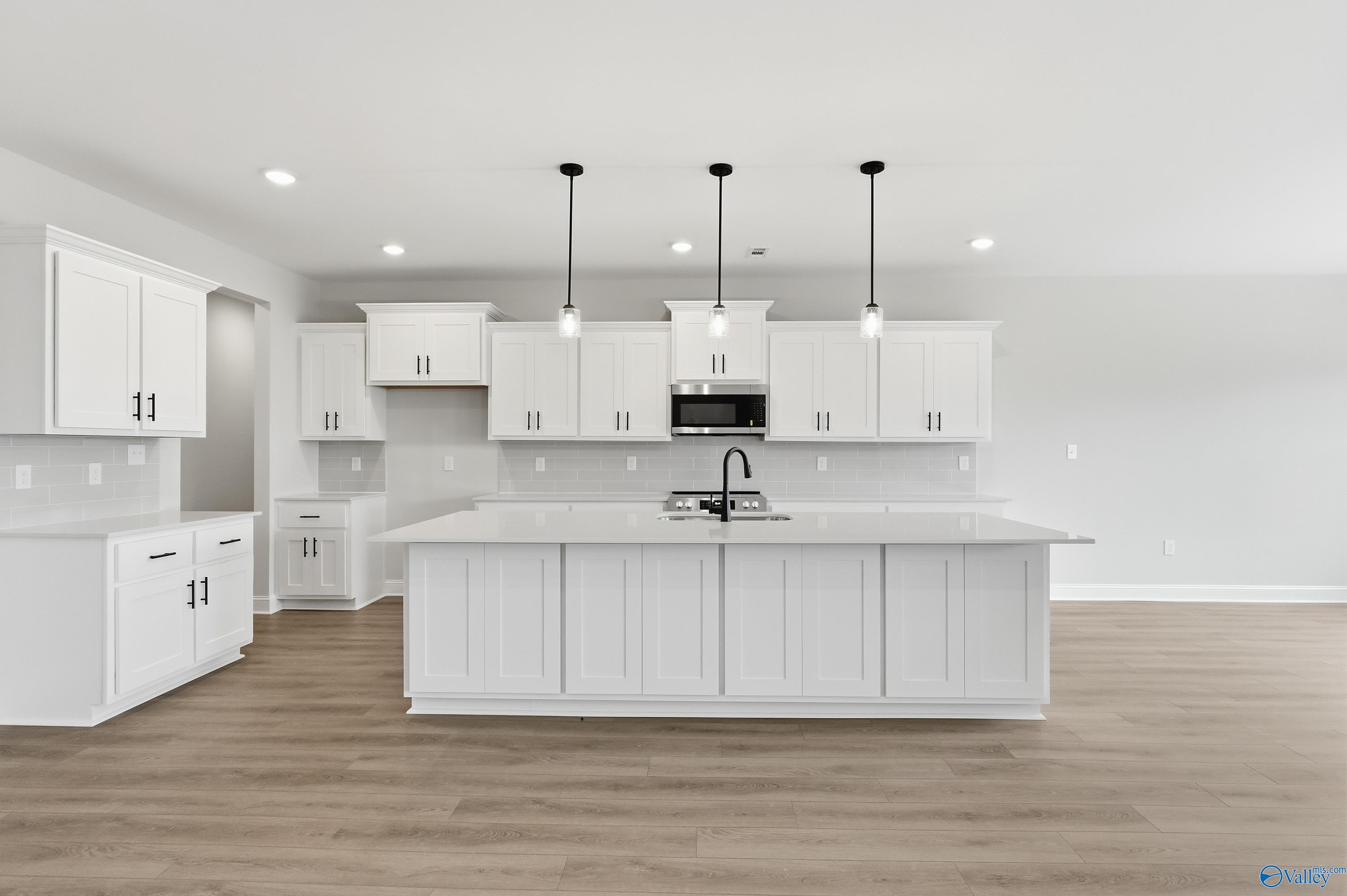 Bright white kitchen with large island, pendant lights, and hardwood floors in 3-bedroom The Finleigh home, Meridianville, Alabama