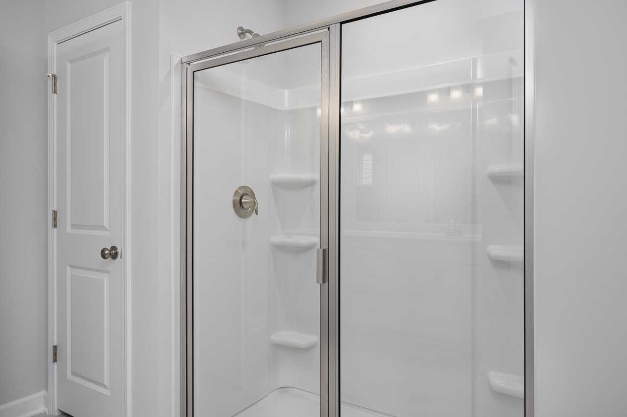 Spacious white tiled walk-in shower in The Durham D master suite bathroom with glass enclosure and shelves