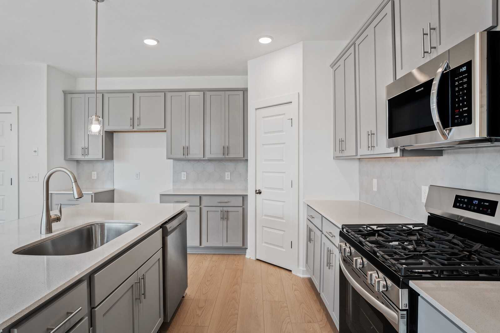 Modern gray shaker kitchen with stainless appliances, subway tile backsplash, and island in Davidson Homes The Logan B, White House, TN