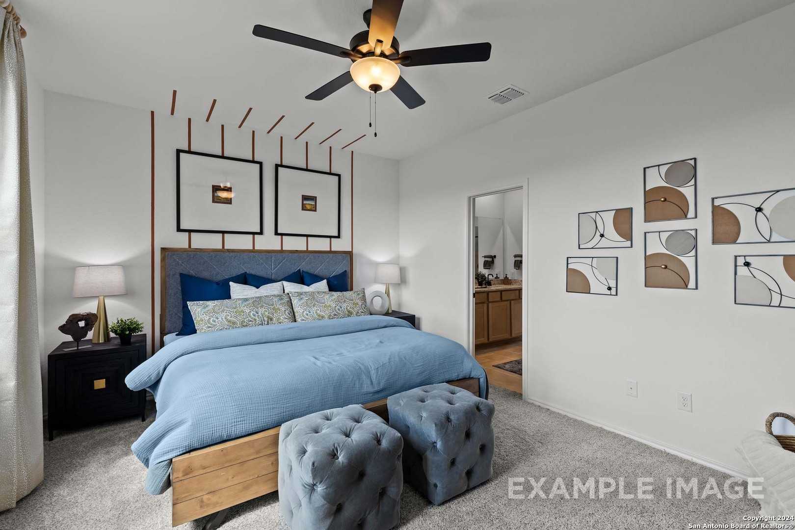 Serene master bedroom with blue king bed, wooden frame, tufted ottomans, ceiling fan, and abstract art in Davidson Homes The Douglas G, Bricewood, San Antonio