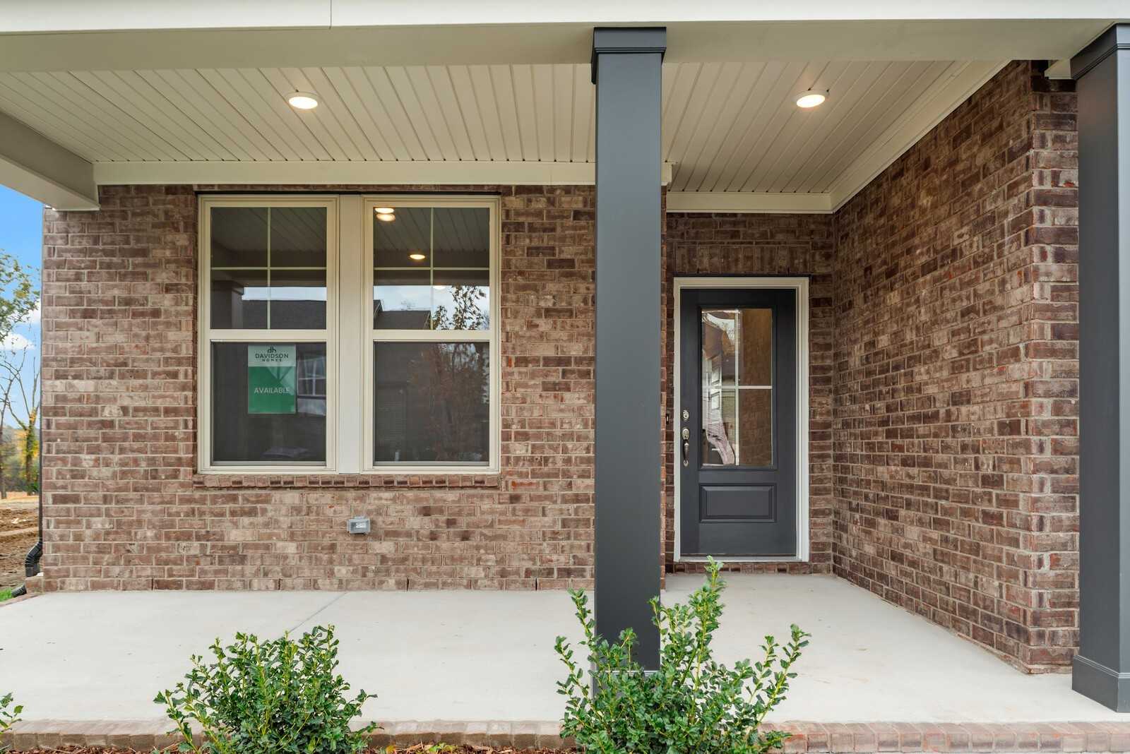 Brick-front two-story home with covered porch, large windows, and dark gray door in Davidson Homes The Henry B, Gallatin, Tennessee