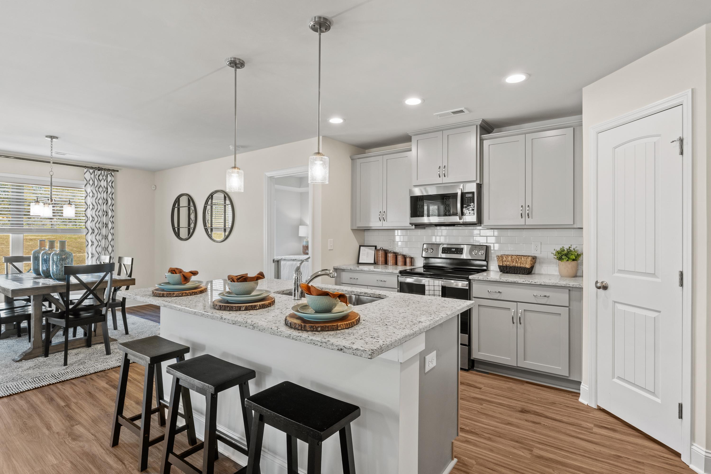 Spacious open-concept kitchen in Berry Cove home, New Market AL with gray shaker cabinets, granite island, stainless appliances, hardwood floors