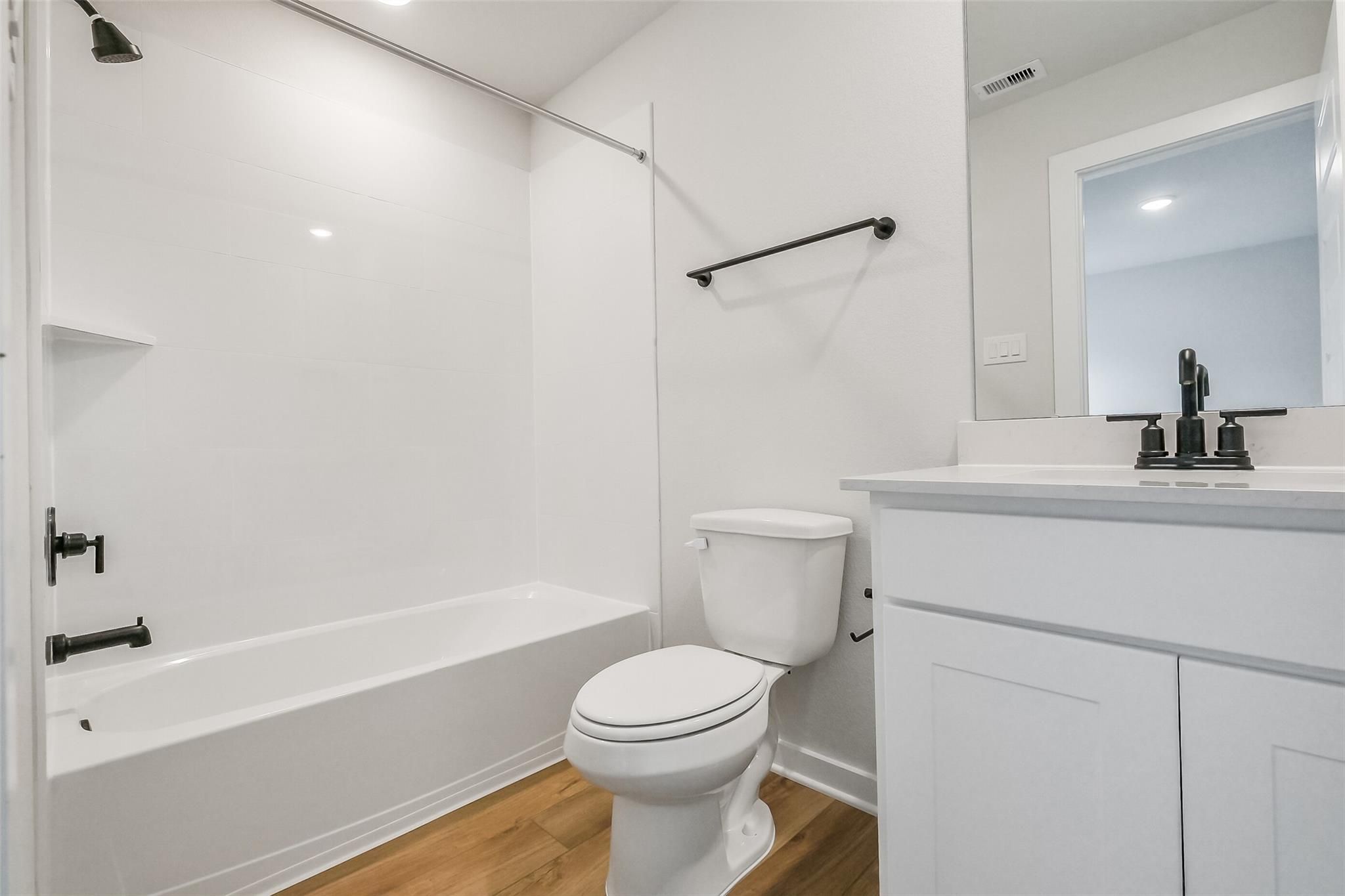 Modern bathroom with tub-shower combo, white vanity sink, toilet, and hardwood floors in Davidson Homes The Tierra B, Beasley, Texas