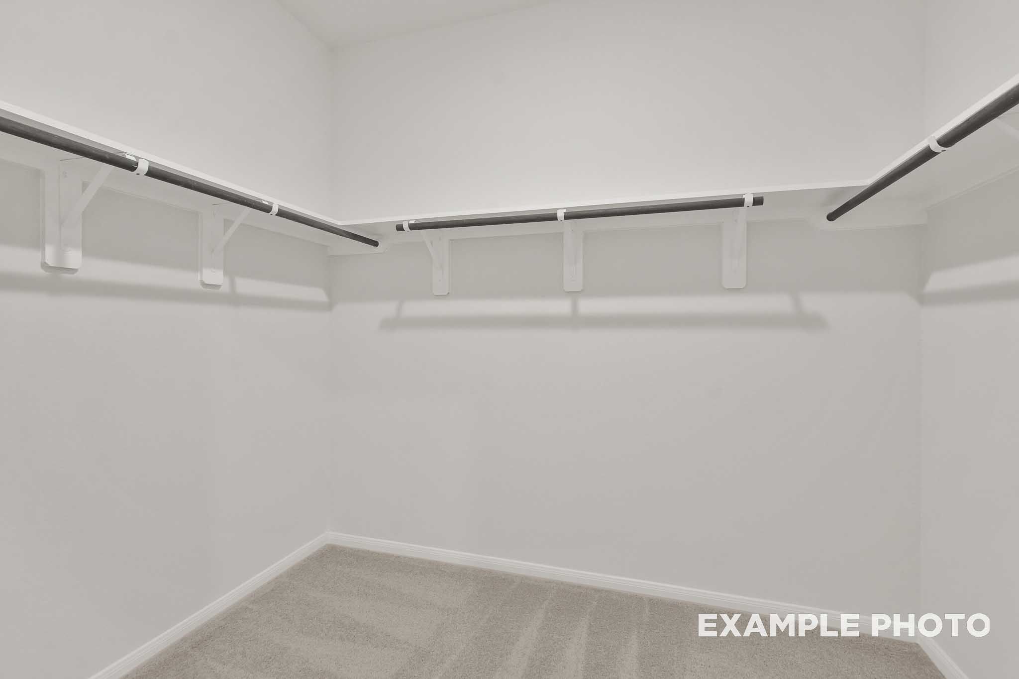 Spacious walk-in closet with white shelving and hanging rods in The Brazos by Davidson Homes, Beasley, Texas.