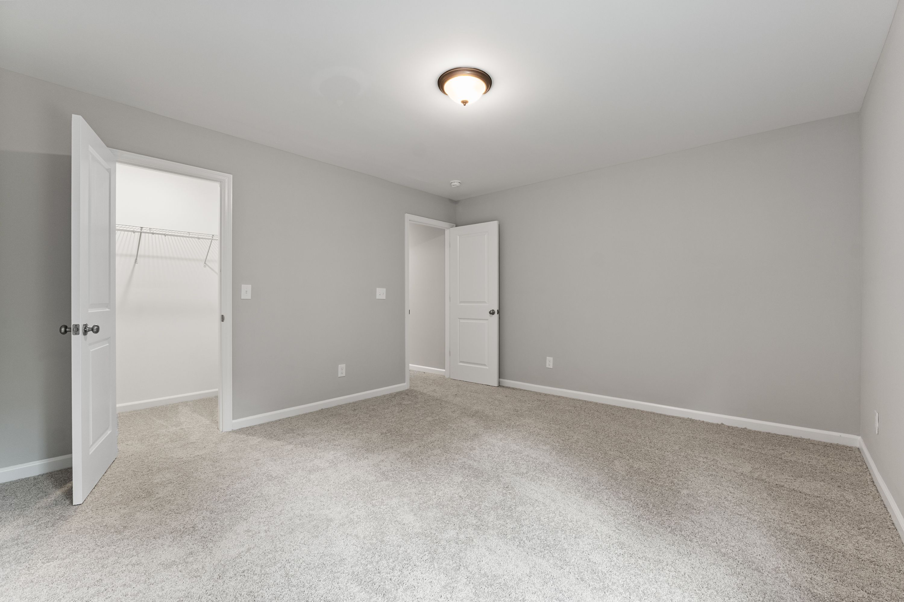 Spacious master bedroom in The Avalon E with light gray walls, walk-in closet, and open doors on carpeted floor