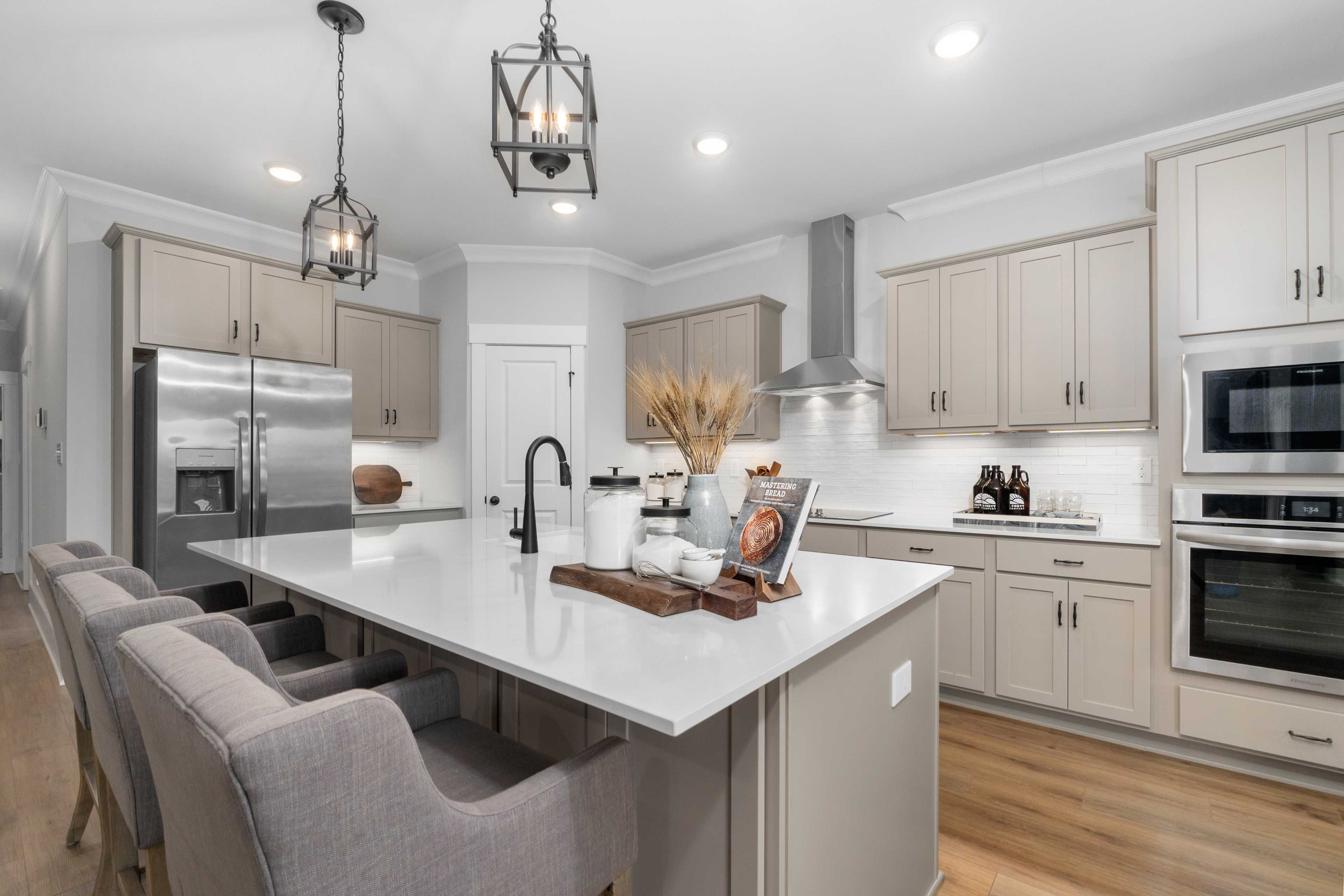 Modern kitchen at Kendall Farms in Toney AL featuring shaker cabinets, white quartz island with bar seating, and stainless appliances