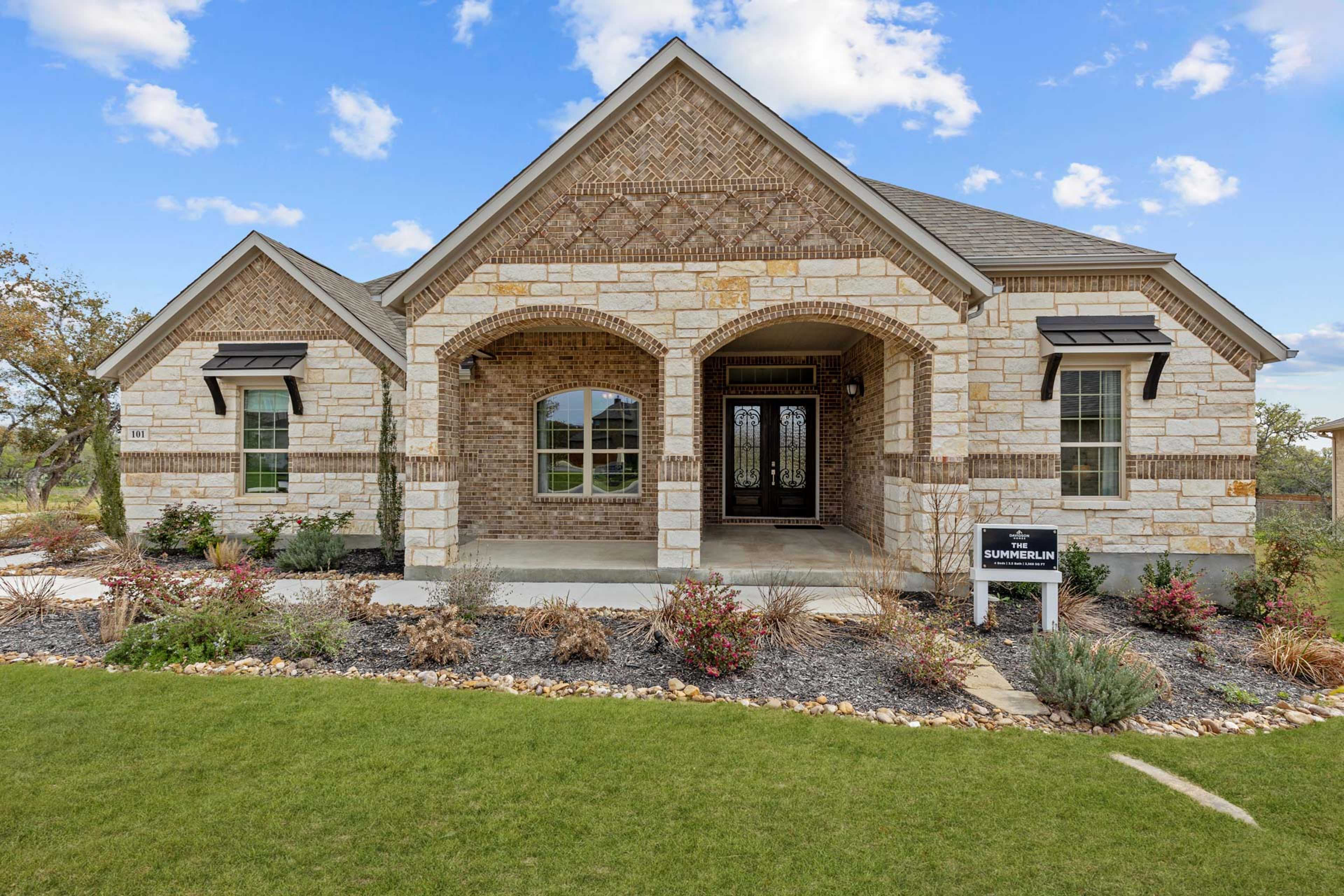 Brick stone home exterior at Potranco Oaks in Castroville Texas with arched entry covered porch and landscaped yard