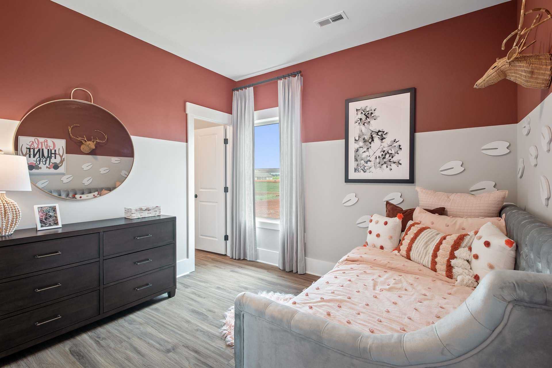 Charming girl's bedroom at Heritage Lakes in New Market Alabama with blush walls, antler mirror, tufted daybed, pillows and hardwood floors