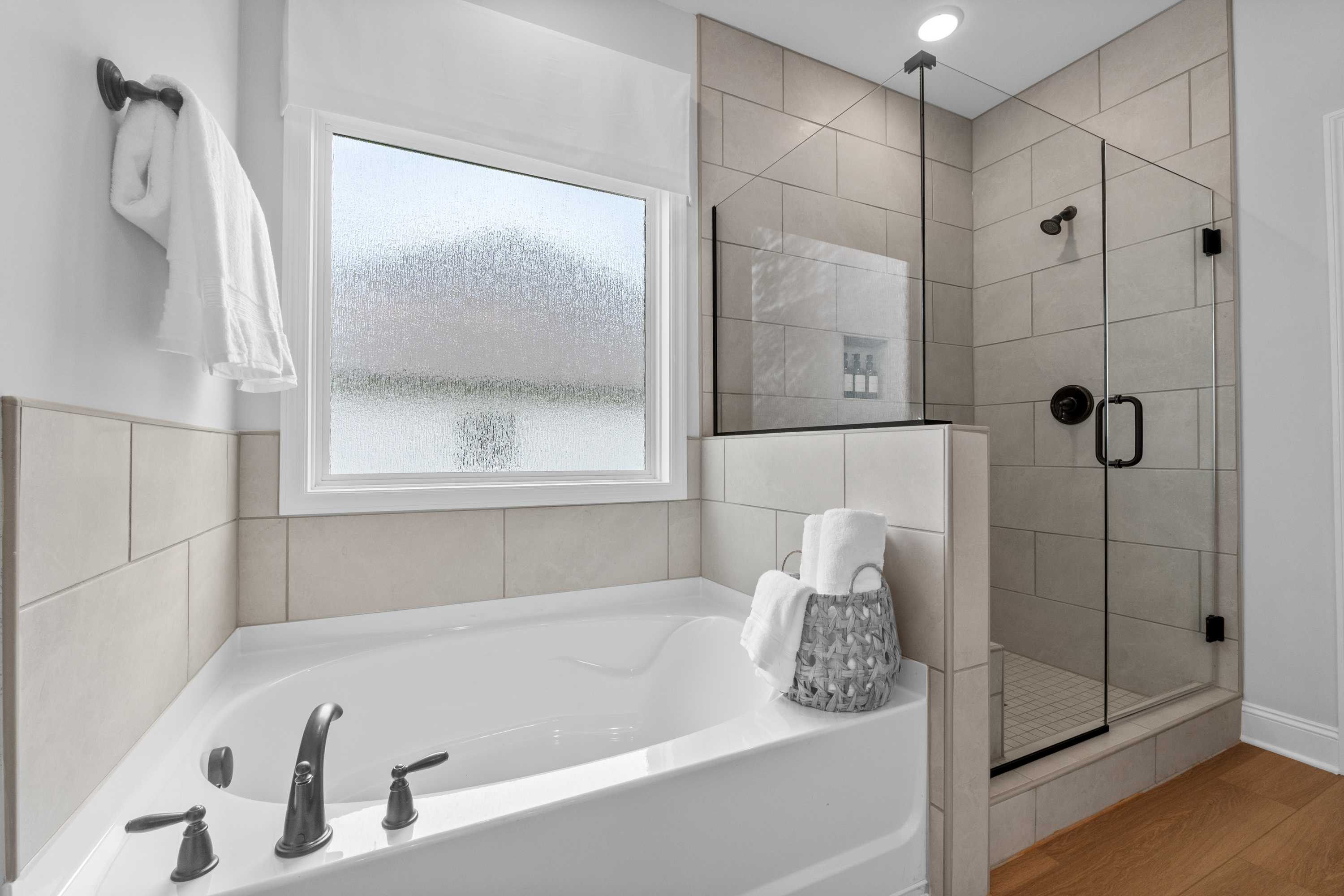 Spacious master bathroom in The Daphne featuring corner soaking tub, frameless glass shower, and neutral tile walls