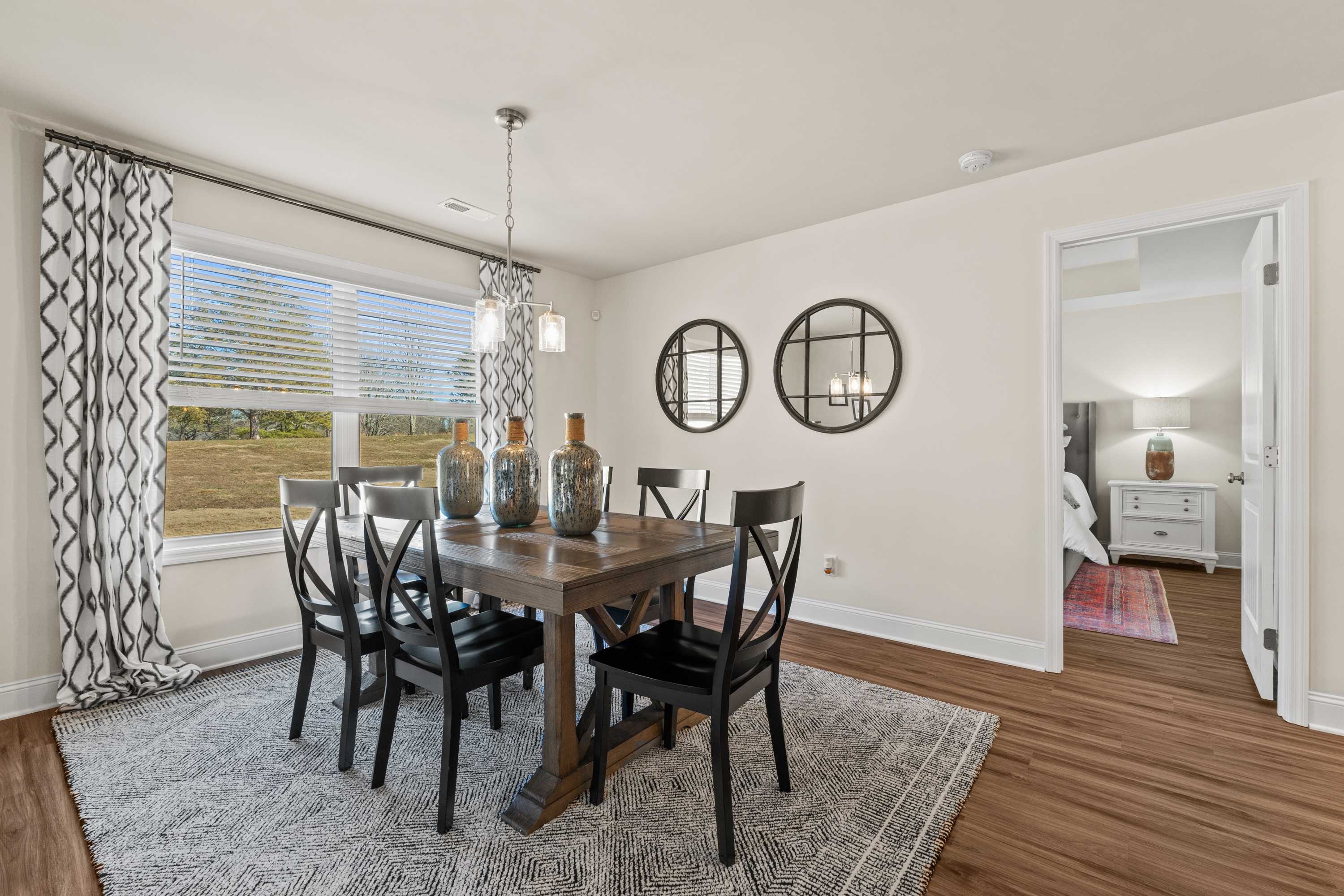 Dining room in Berry Cove, New Market Alabama with rustic wooden table, black chairs, pendant light, and scenic field view through large window