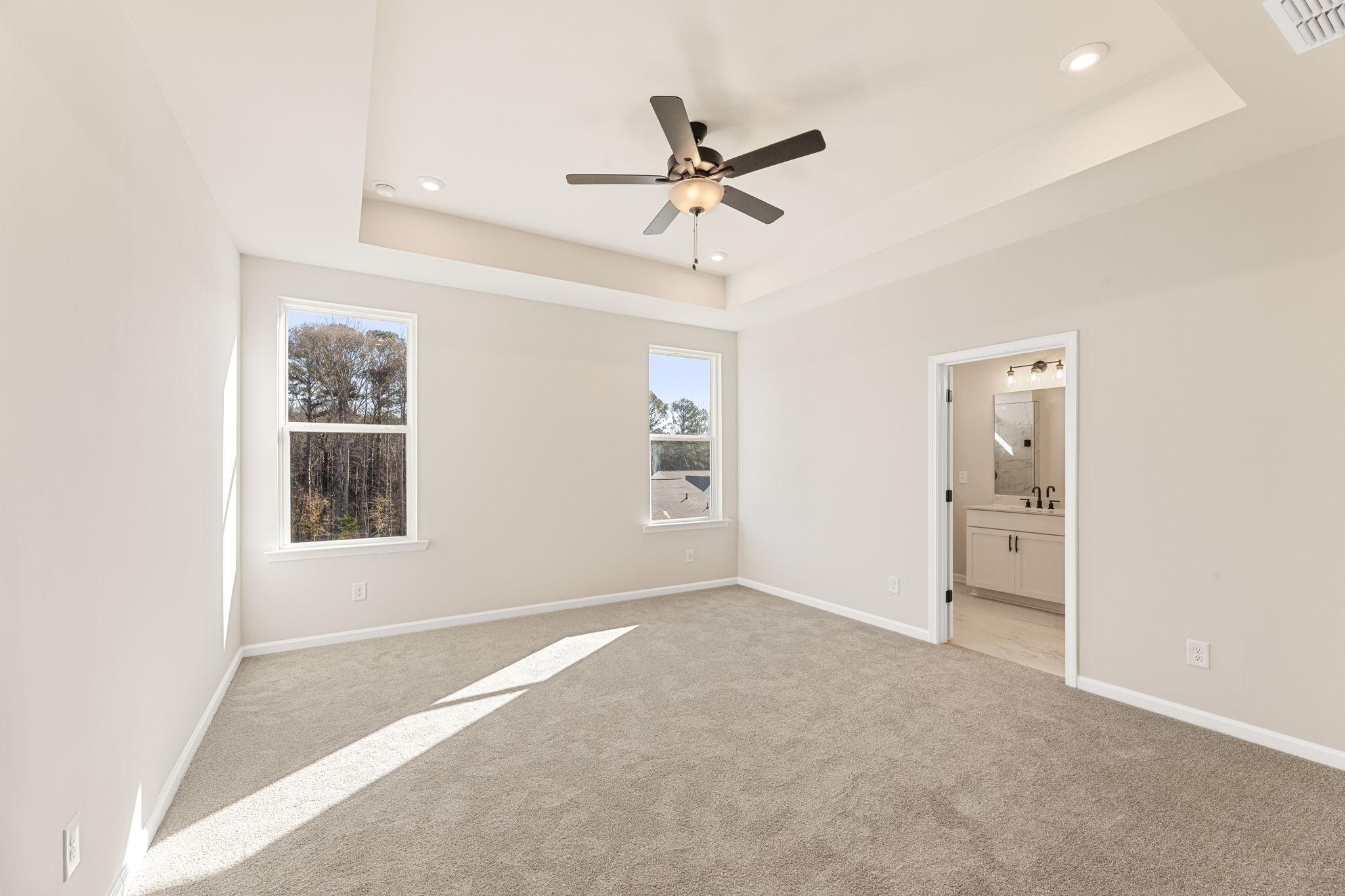 Bright bedroom with large windows, ceiling fan, neutral walls, and en-suite bath in Davidson Homes The Glenwood C, Loganville, GA