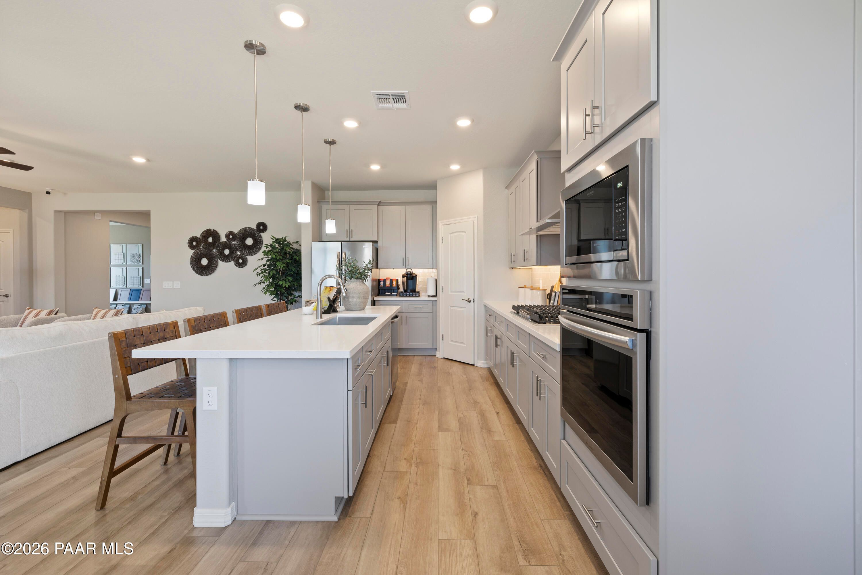 Modern kitchen with white island, stainless appliances, and wood floors in The Harmony A home at Pronghorn Ranch, Prescott.