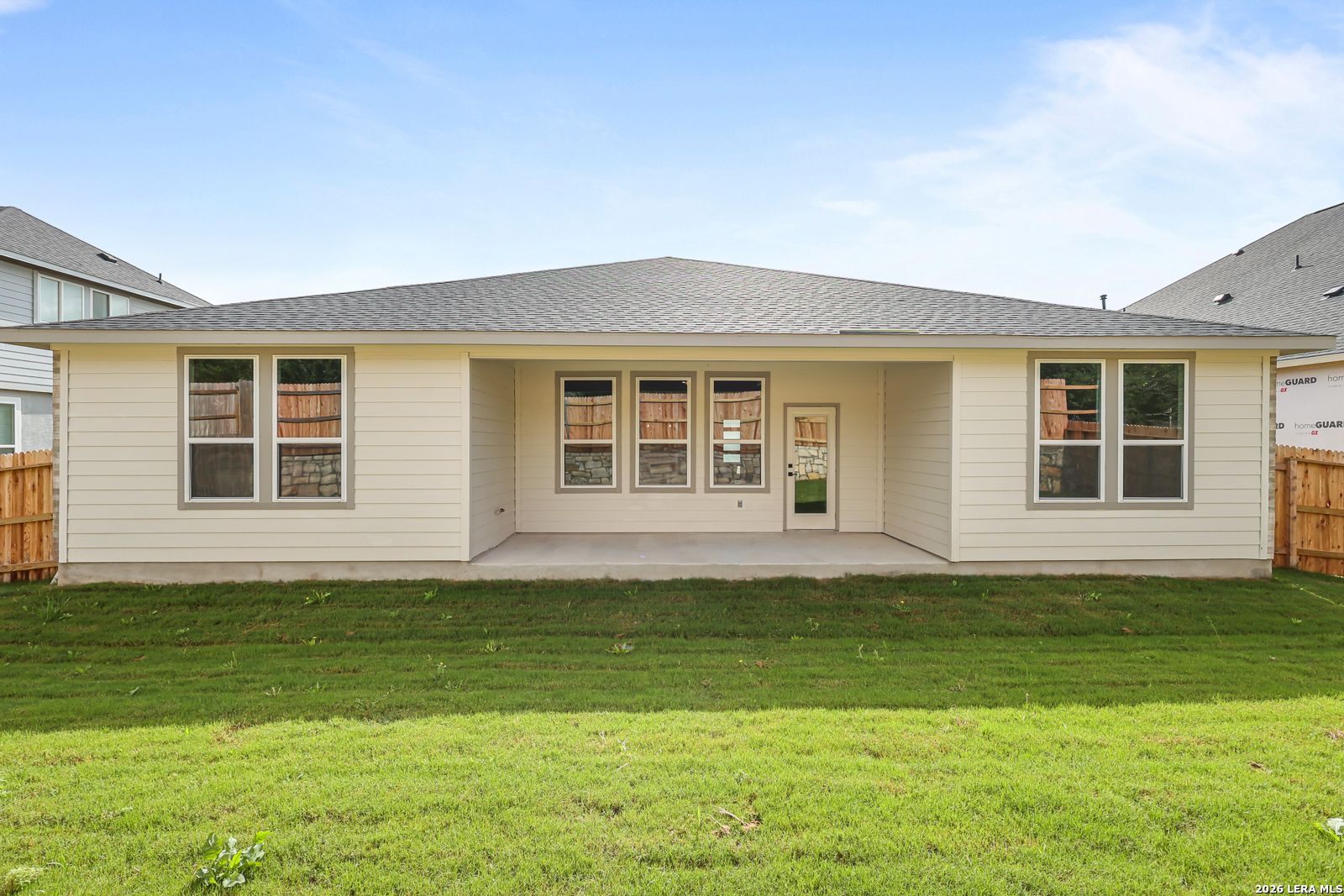 Back view of The Lanier G single-story home with covered patio, large windows, and lush green lawn in The Reserve at Potranco Oaks, Castroville, Texas