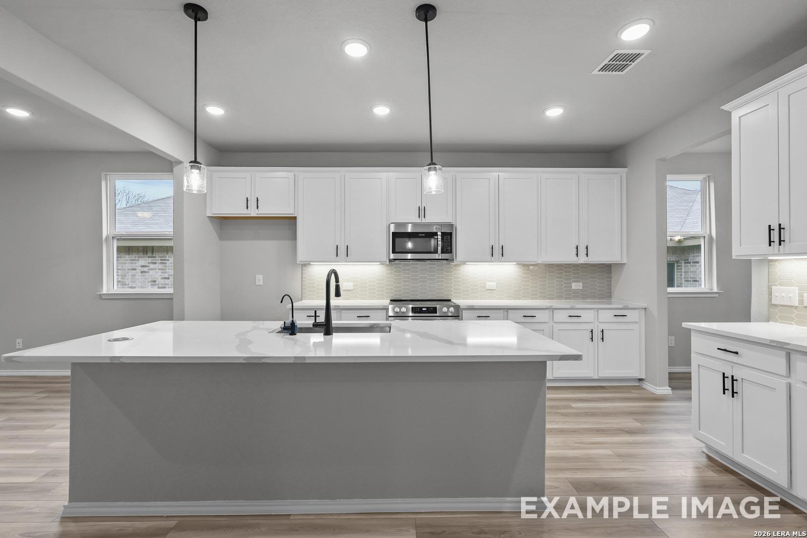 Modern white kitchen with quartz island, pendant lighting, and stainless appliances in The Glenwood E, Royal Crest, TX.