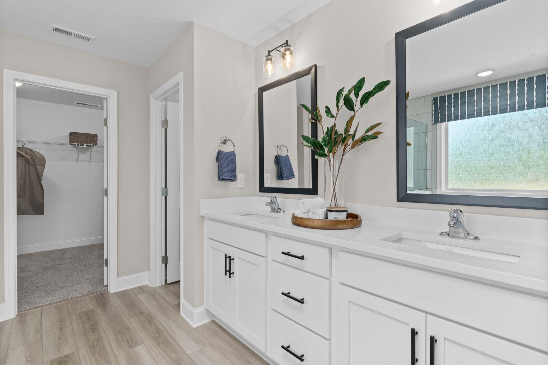 Spacious master bathroom at Creek Grove in New Market AL with double white vanity, black-framed mirrors, and hardwood floors