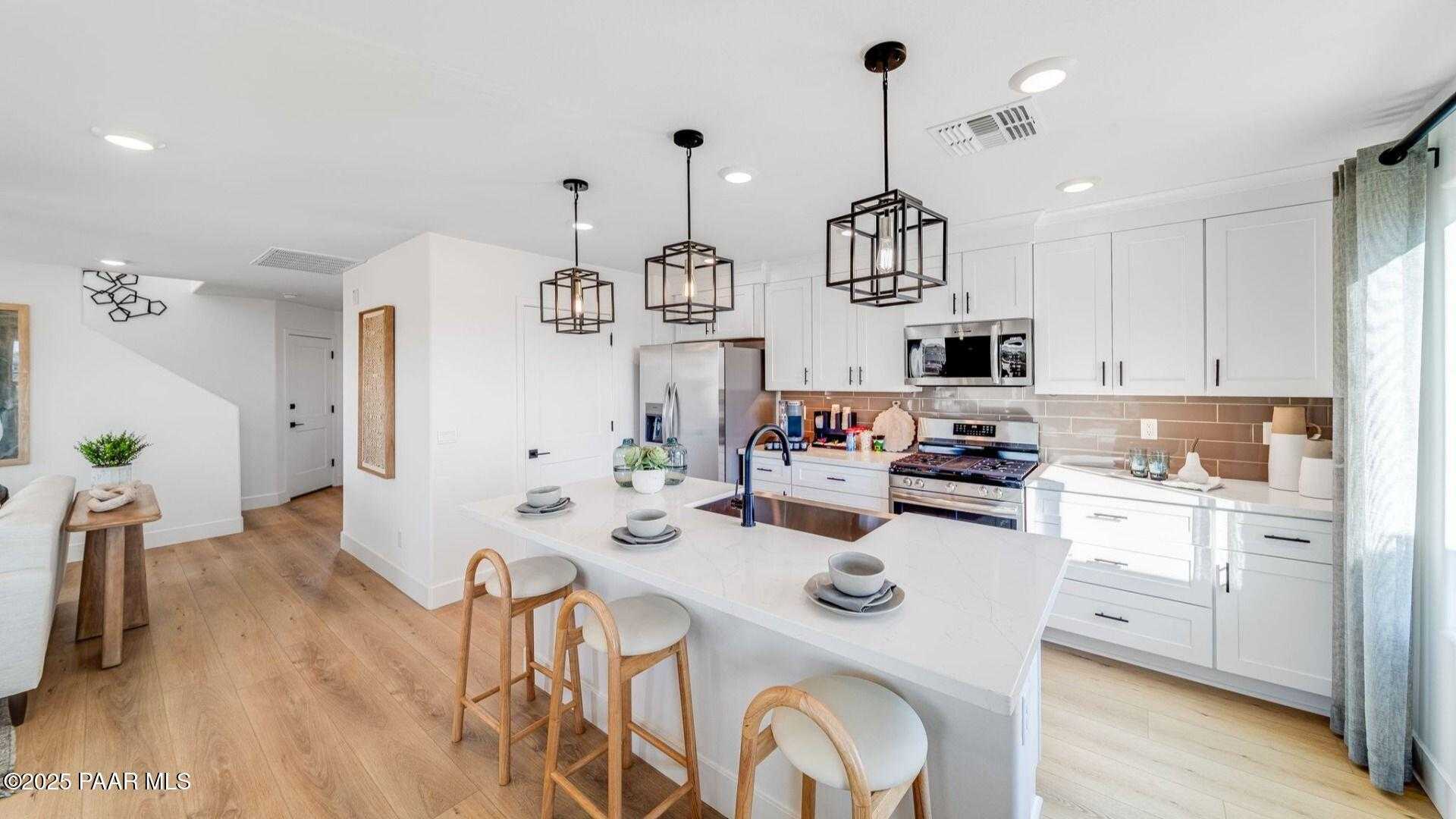 Modern open-concept kitchen with white cabinets, large island, pendant lights, and stainless appliances in Davidson Homes Wilmington B, Prescott AZ