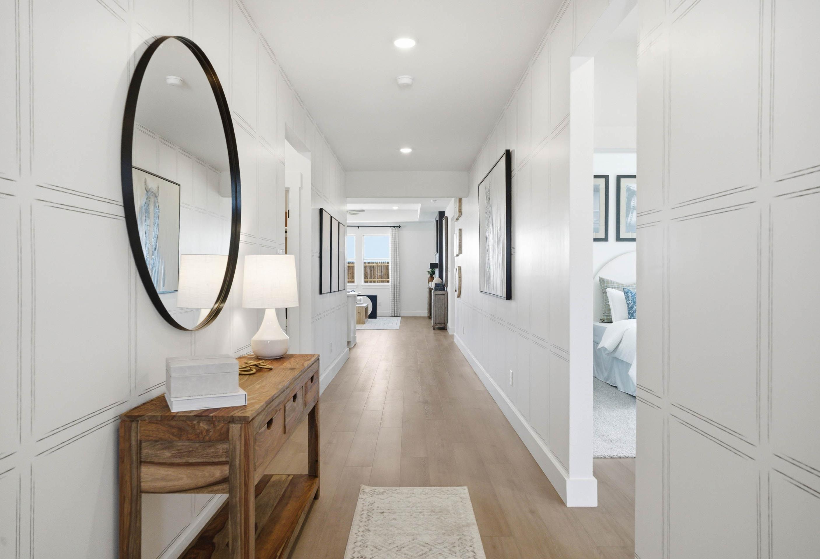 Bright hallway in The Laurel M home design featuring elegant board and batten walls, wood console table, and oval mirror.