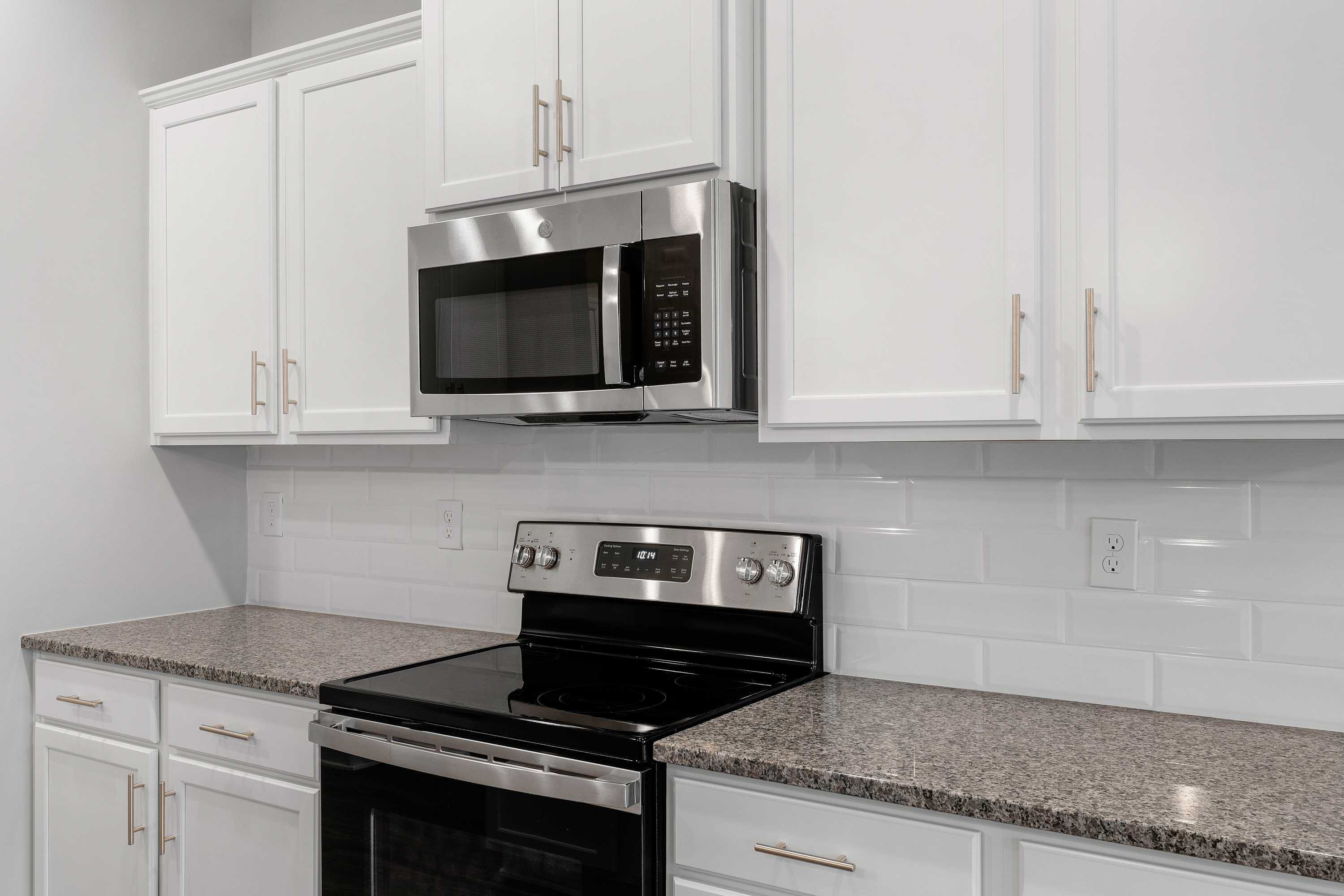 The Aiken kitchen by Davidson Homes featuring white shaker cabinets, stainless steel microwave and oven, granite counters, subway tile backsplash