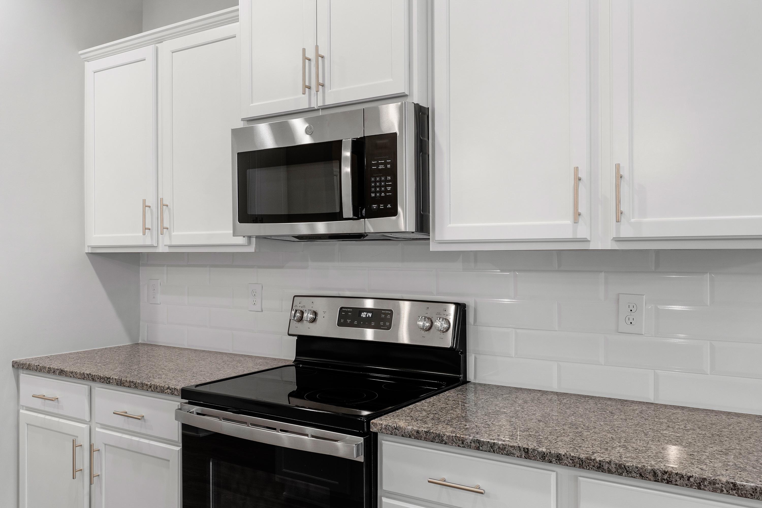 The Aiken kitchen by Davidson Homes featuring white shaker cabinets, stainless steel microwave and oven, granite counters, subway tile backsplash