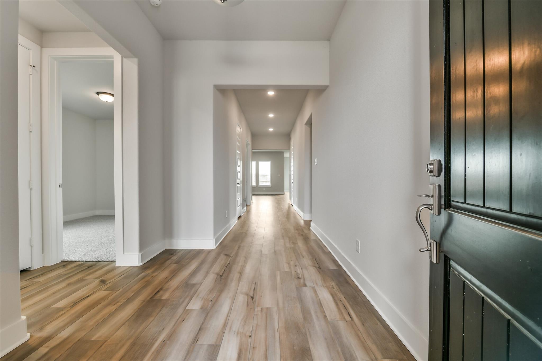 Bright hallway with light oak floors, white walls, and recessed lighting in Davidson Homes The George A, Lago Mar, Texas City