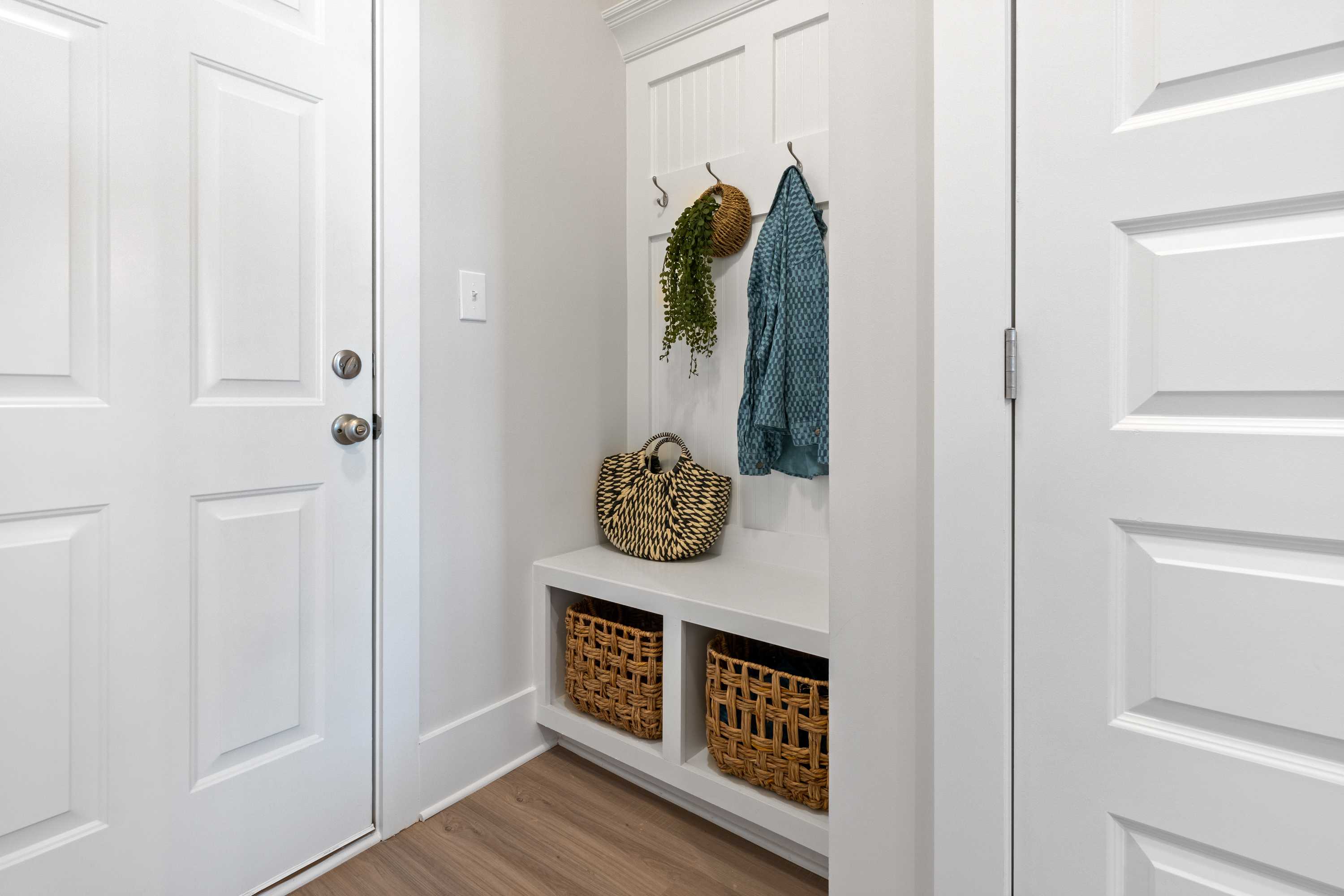 Spacious Chelsea A mudroom with built-in white bench, wicker baskets, coat hooks holding fern and blue jacket