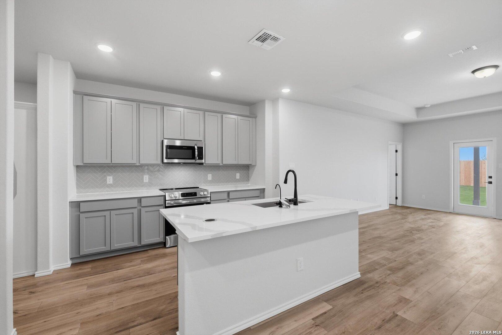 Modern kitchen with white quartz island, gray shaker cabinets, stainless appliances, subway tile backsplash in The Blanco C, San Antonio