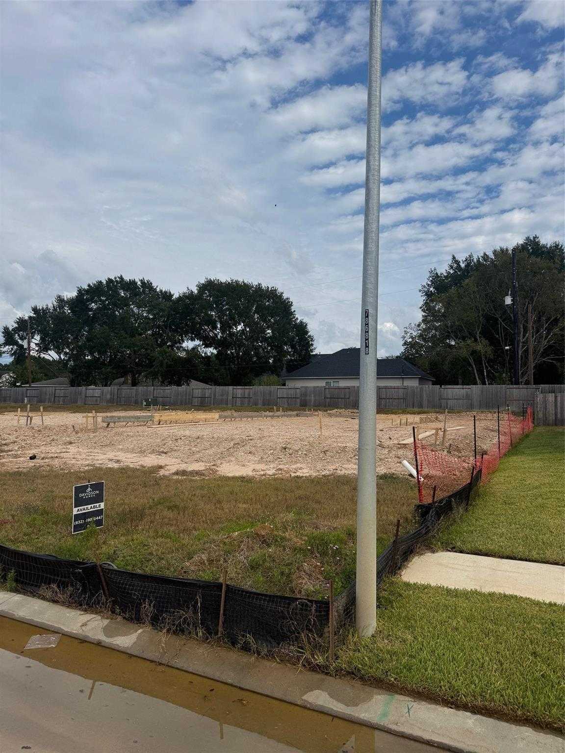 Cleared construction lot with fencing, for-sale sign, and oak trees for Davidson Homes Sabine F in Windmill Estates, Magnolia, Texas