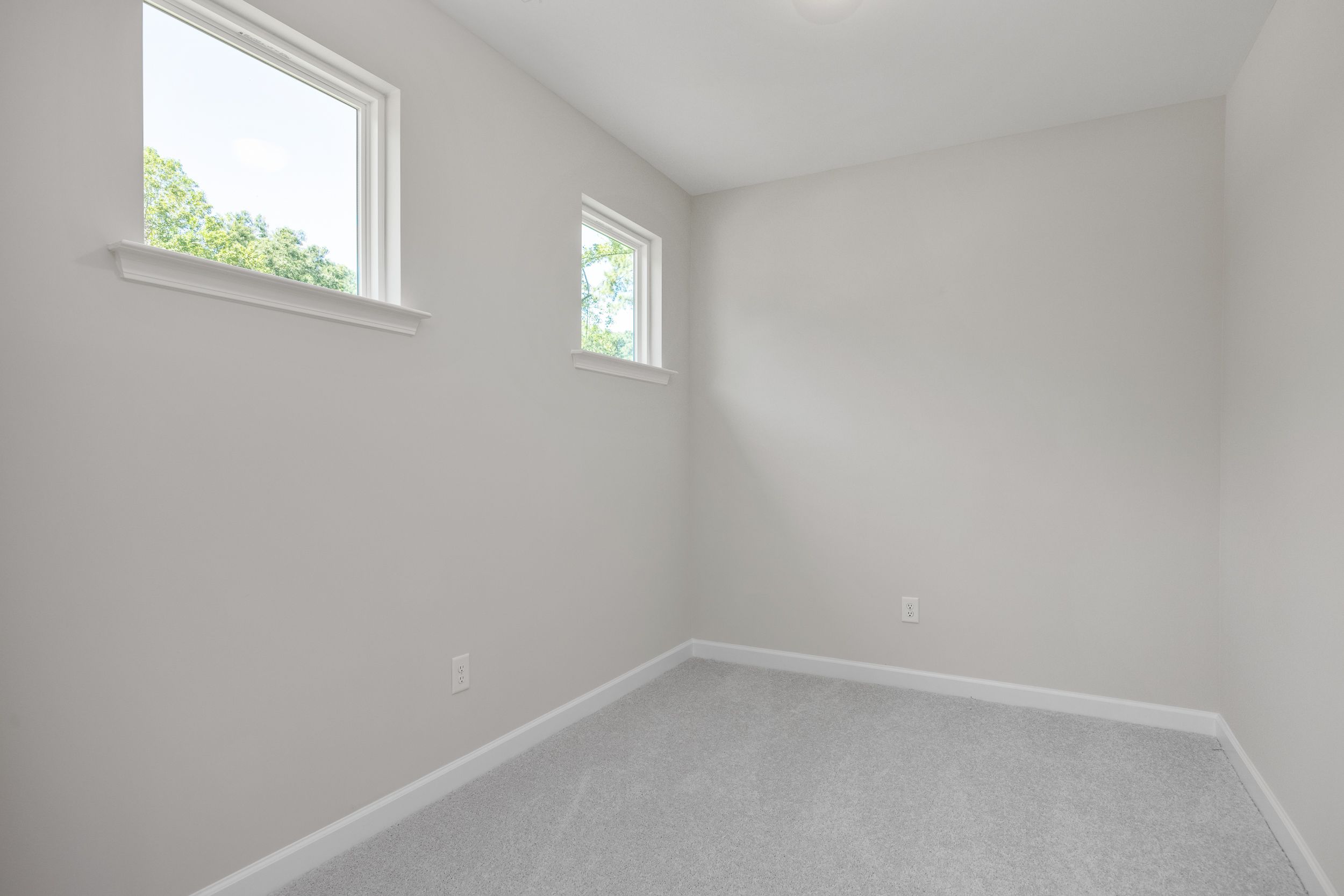 Bright upper floor bedroom in The Aspen C home design, featuring gray walls, beige carpet, and large windows with tree views