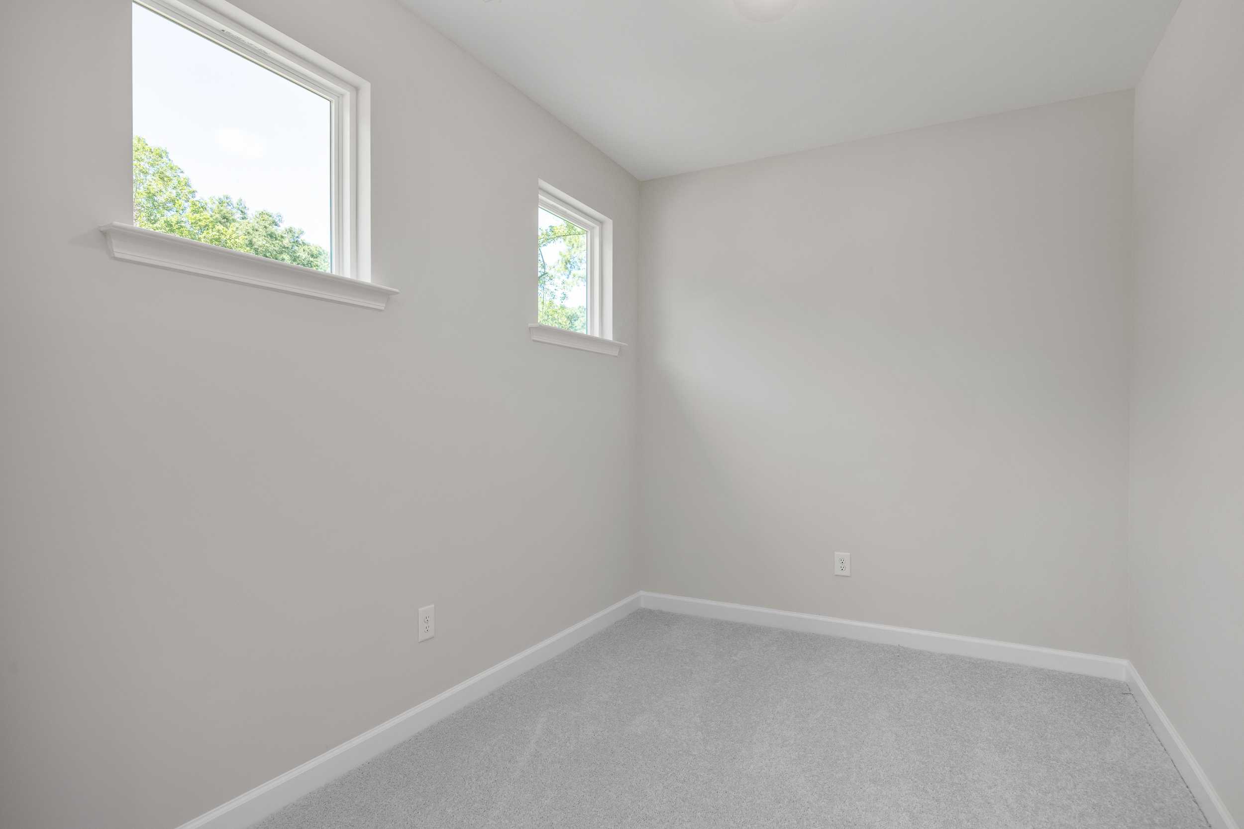 Bright upper floor bedroom in The Aspen C home design, featuring gray walls, beige carpet, and large windows with tree views