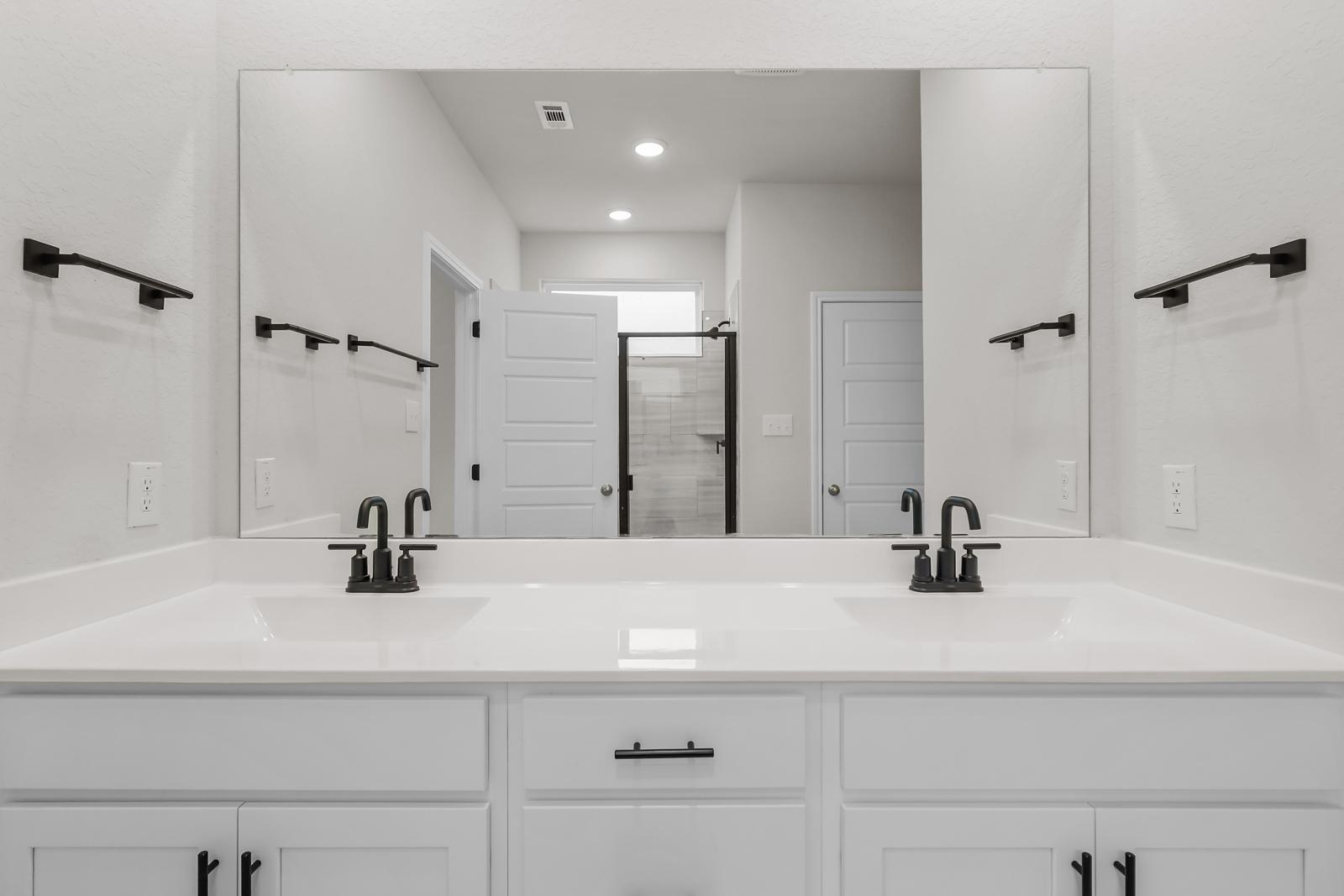 Modern primary bathroom vanity in The Sequoia C featuring dual sinks, matte black fixtures, and white cabinetry.