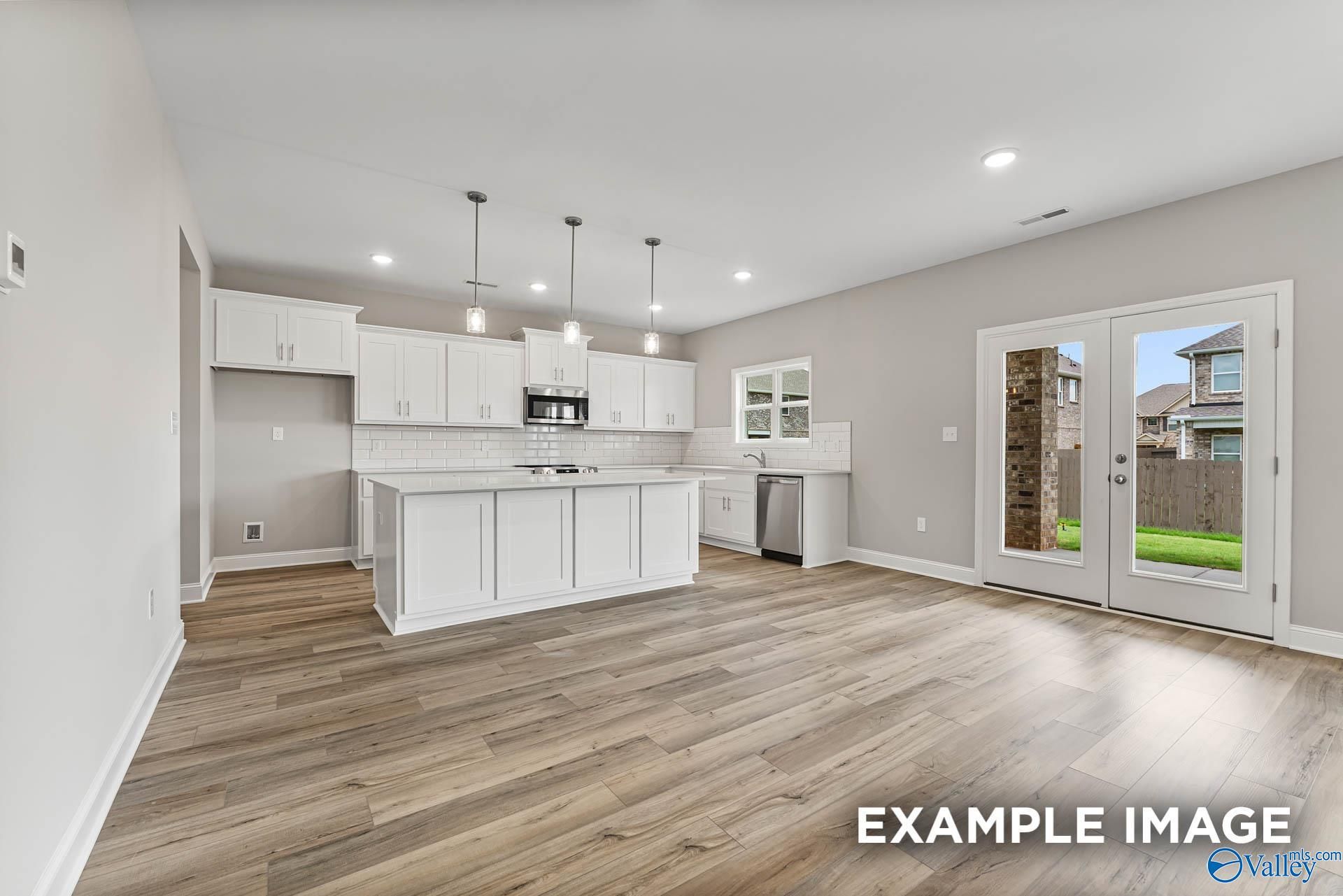 Modern white kitchen with large island, stainless appliances, wood floors, and sliding doors to backyard in Davidson Homes Chelsea A, Athens AL