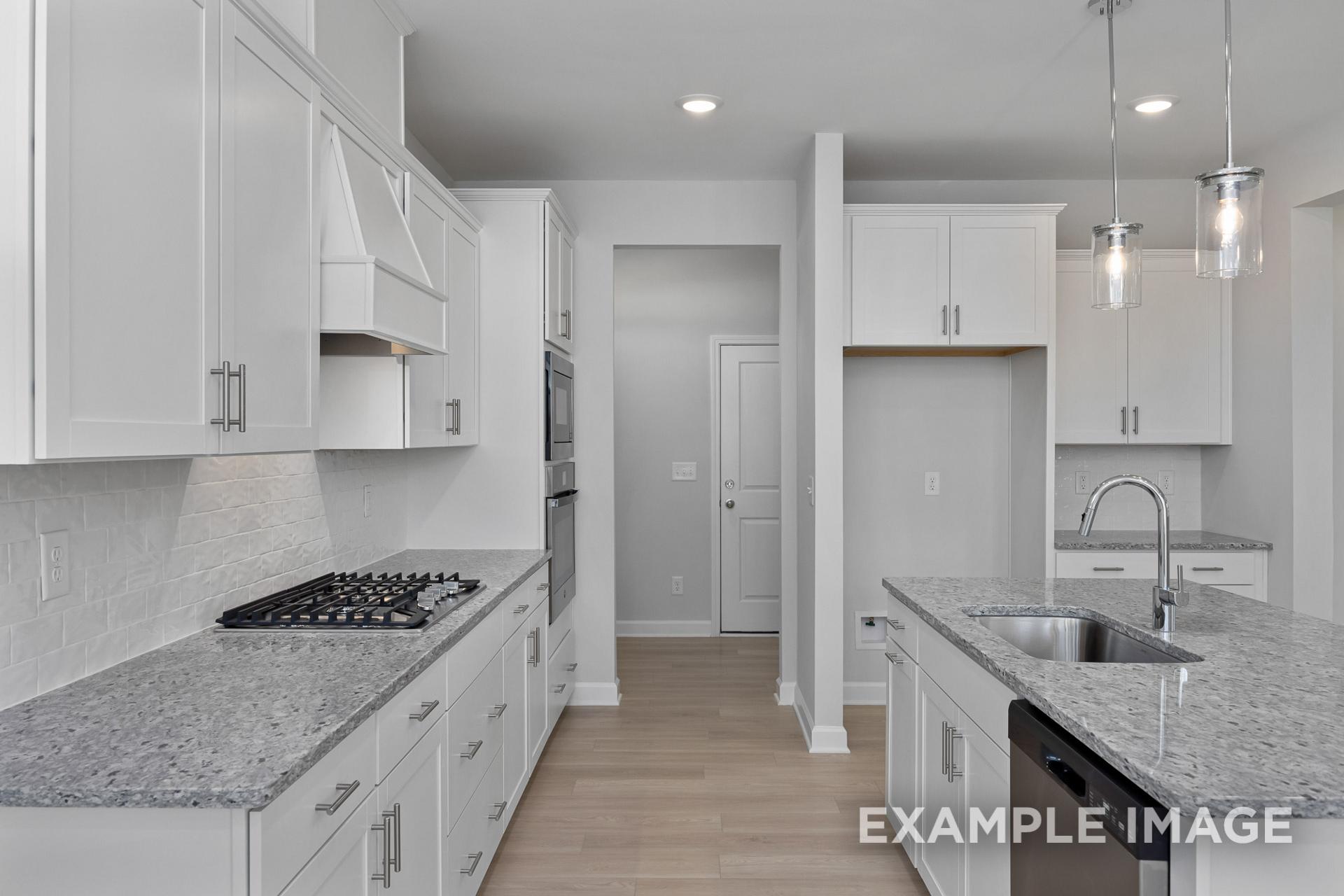 Modern kitchen in The Gavin B by Davidson Homes featuring white cabinetry, granite island, and stainless appliances in Lillington NC