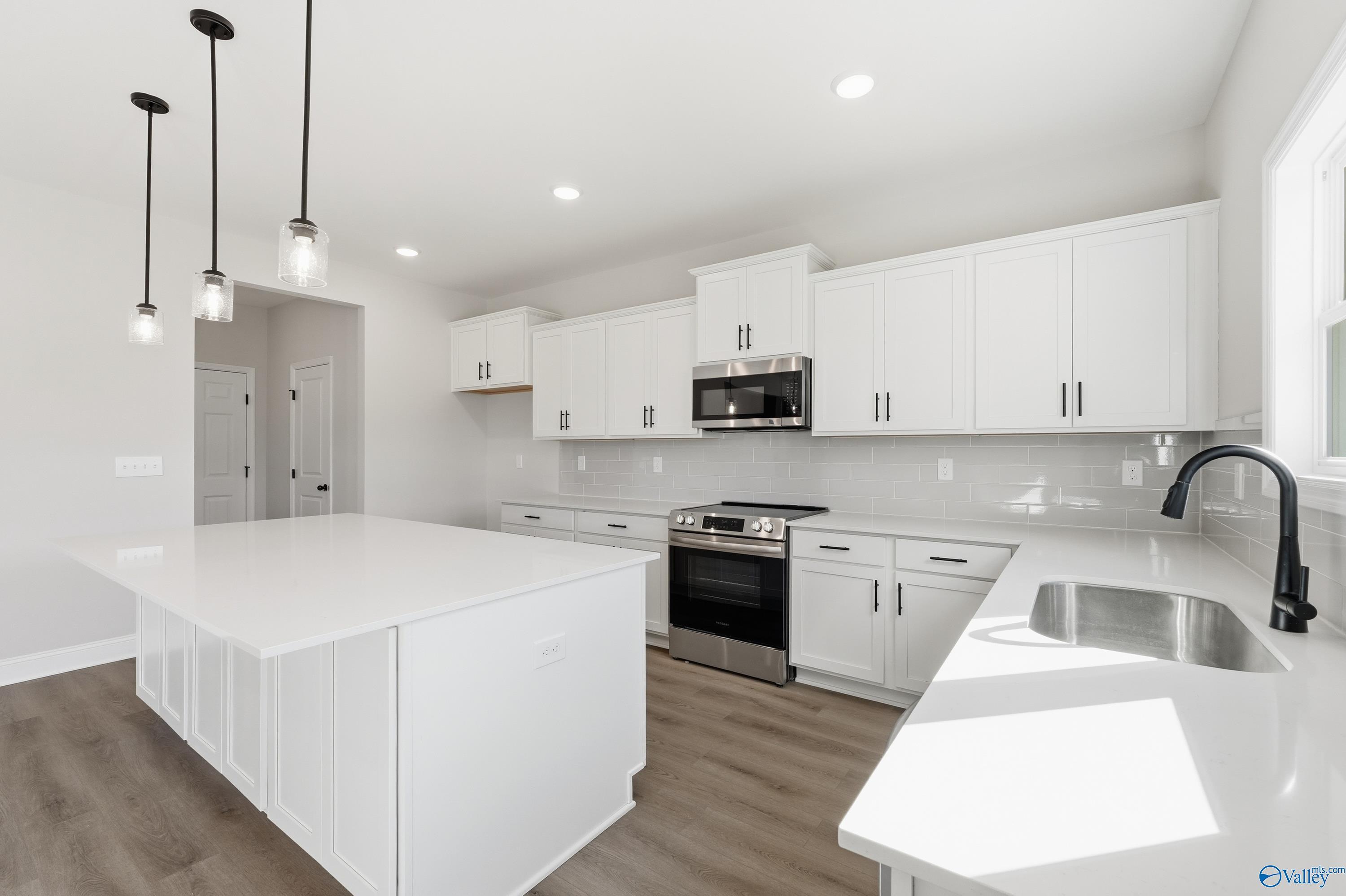 Modern white kitchen featuring large island, shaker cabinets, stainless appliances, and pendant lights in Davidson Homes Chelsea C, Harvest, AL