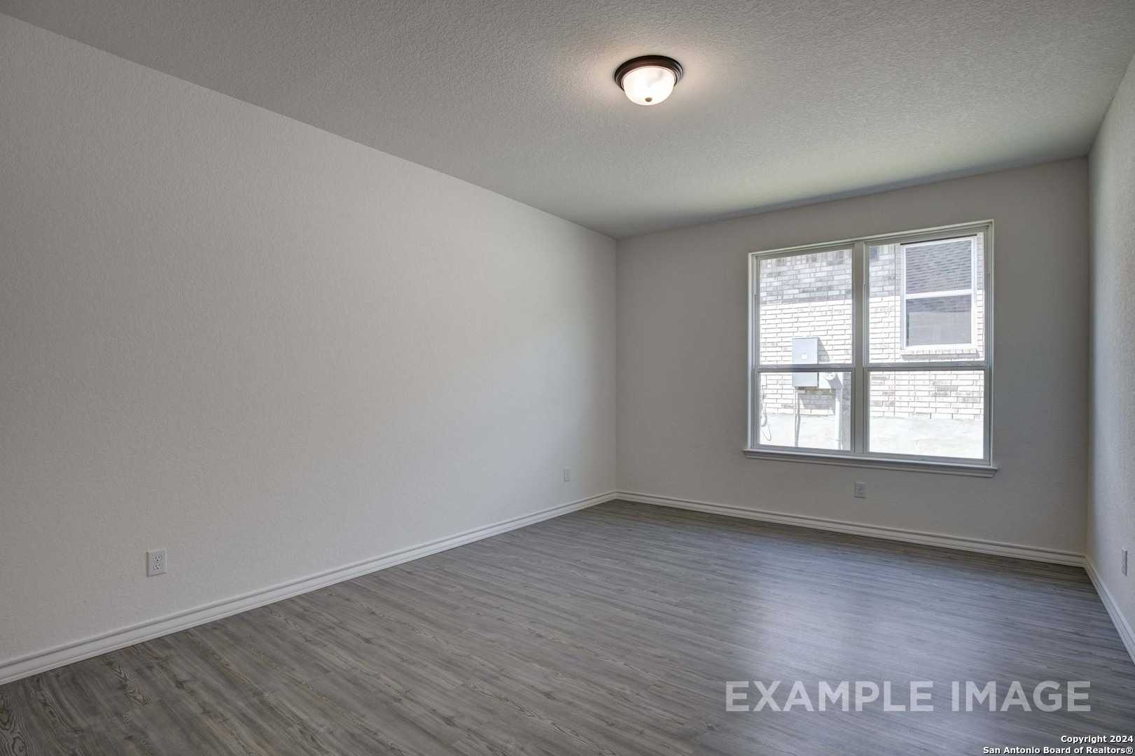 Spacious empty bedroom with large window, white walls, and gray LVP flooring in Davidson Homes The Garner C, Castroville TX