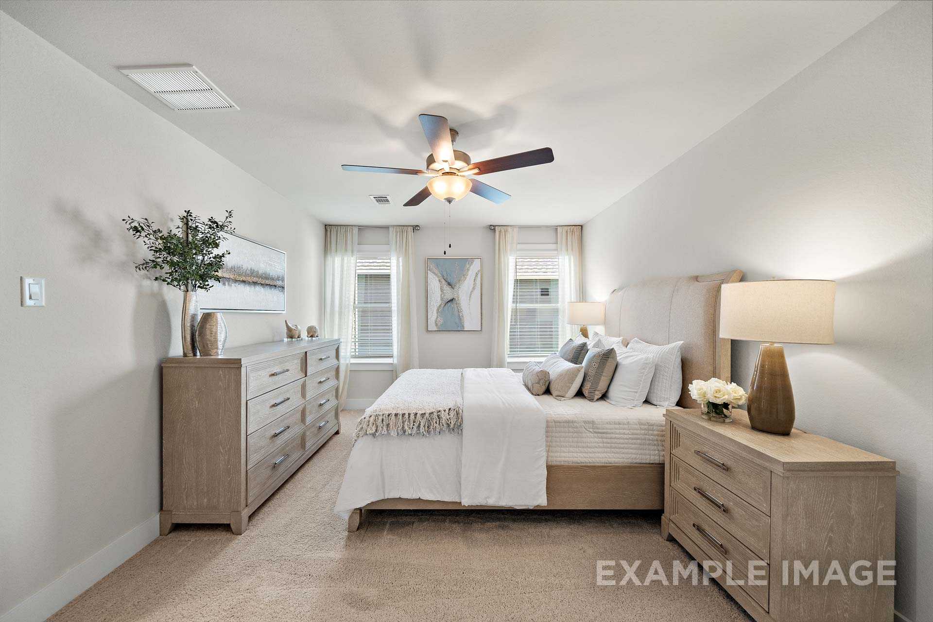 Upper floor master suite in The Lily A featuring king bed, oak dressers, ceiling fan, and sheer-curtained windows