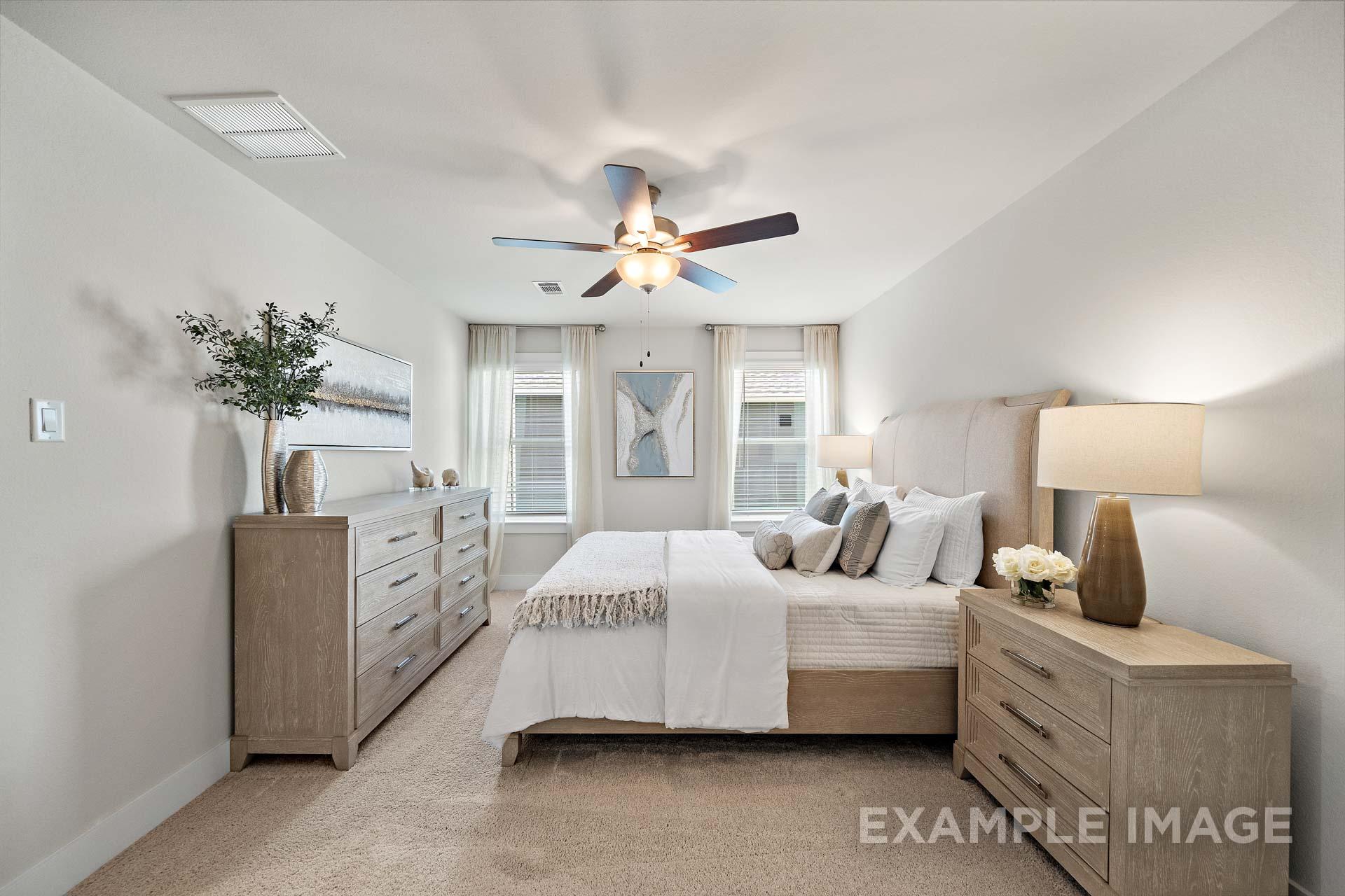 Upper floor master suite in The Lily A featuring king bed, oak dressers, ceiling fan, and sheer-curtained windows