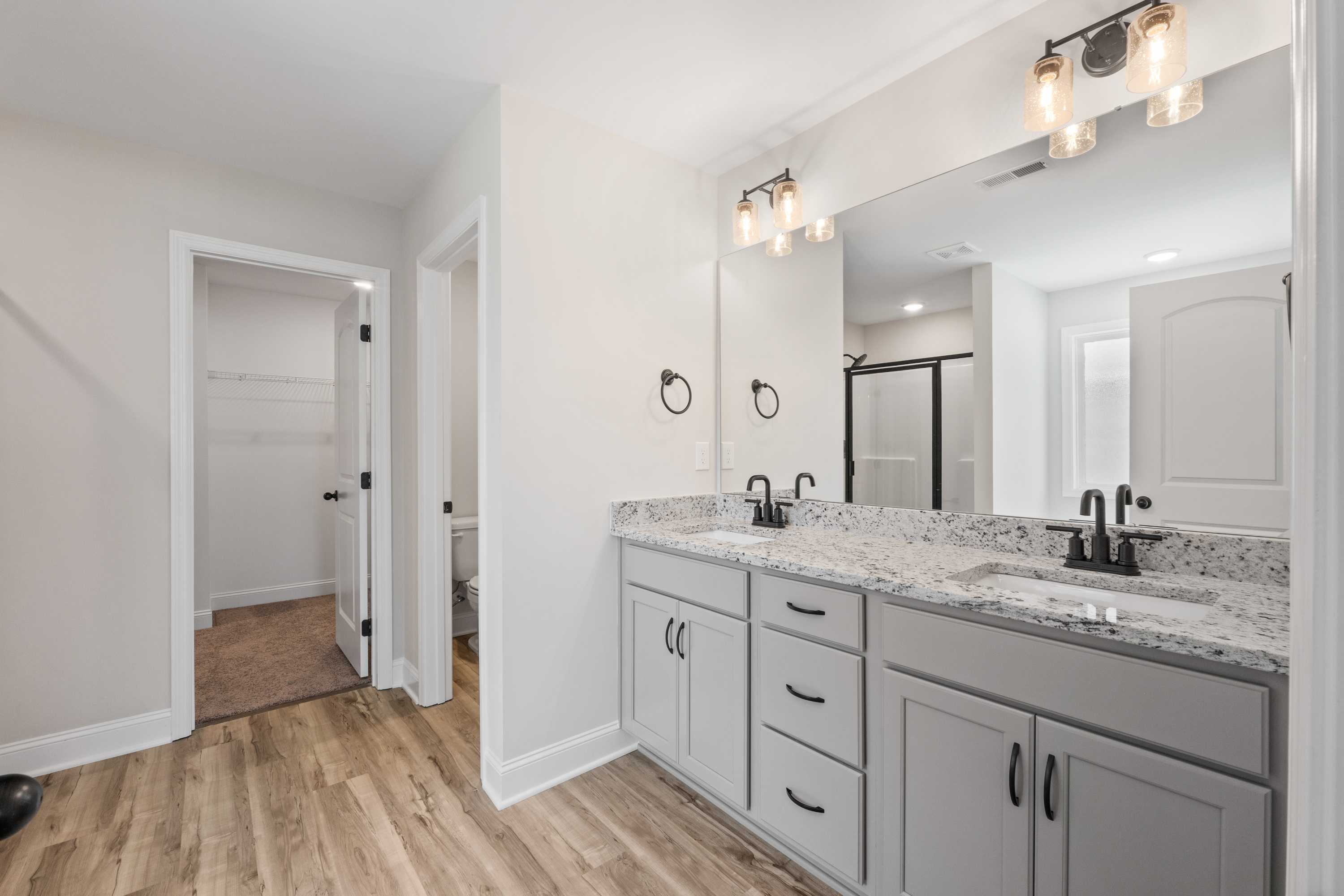 Spacious master bathroom in The Everett C with double gray vanity, quartz counters, large mirror, and closet access