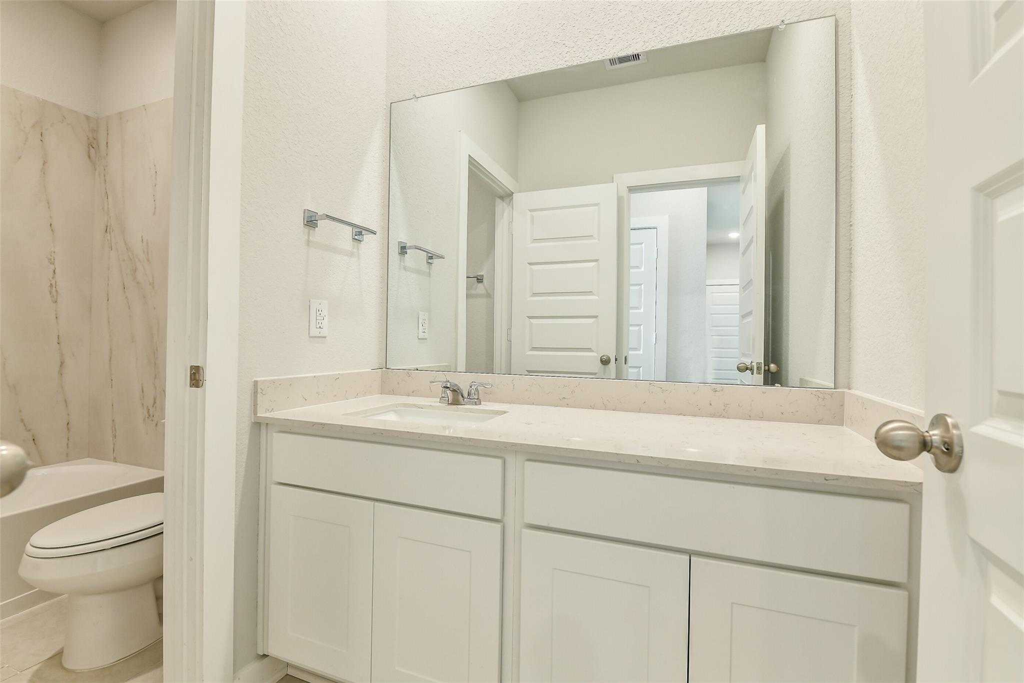 Modern master bathroom with white vanity, large mirror, and enclosed shower-toilet area in Davidson Homes The Colorado F, Cleveland, Texas