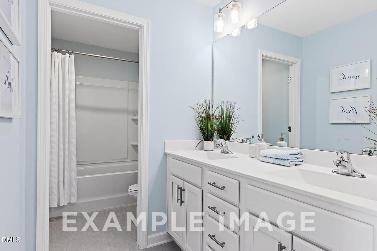 Bright bathroom with double vanity, tub shower combo, and soft blue walls in Davidson Homes The Ash C plan, Lillington NC