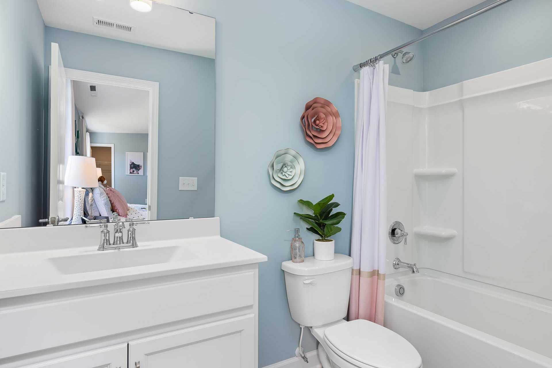 Guest bathroom in Highland Forest Fuquay-Varina NC home with light blue walls, pink floral shower curtain, white vanity sink, and potted plants