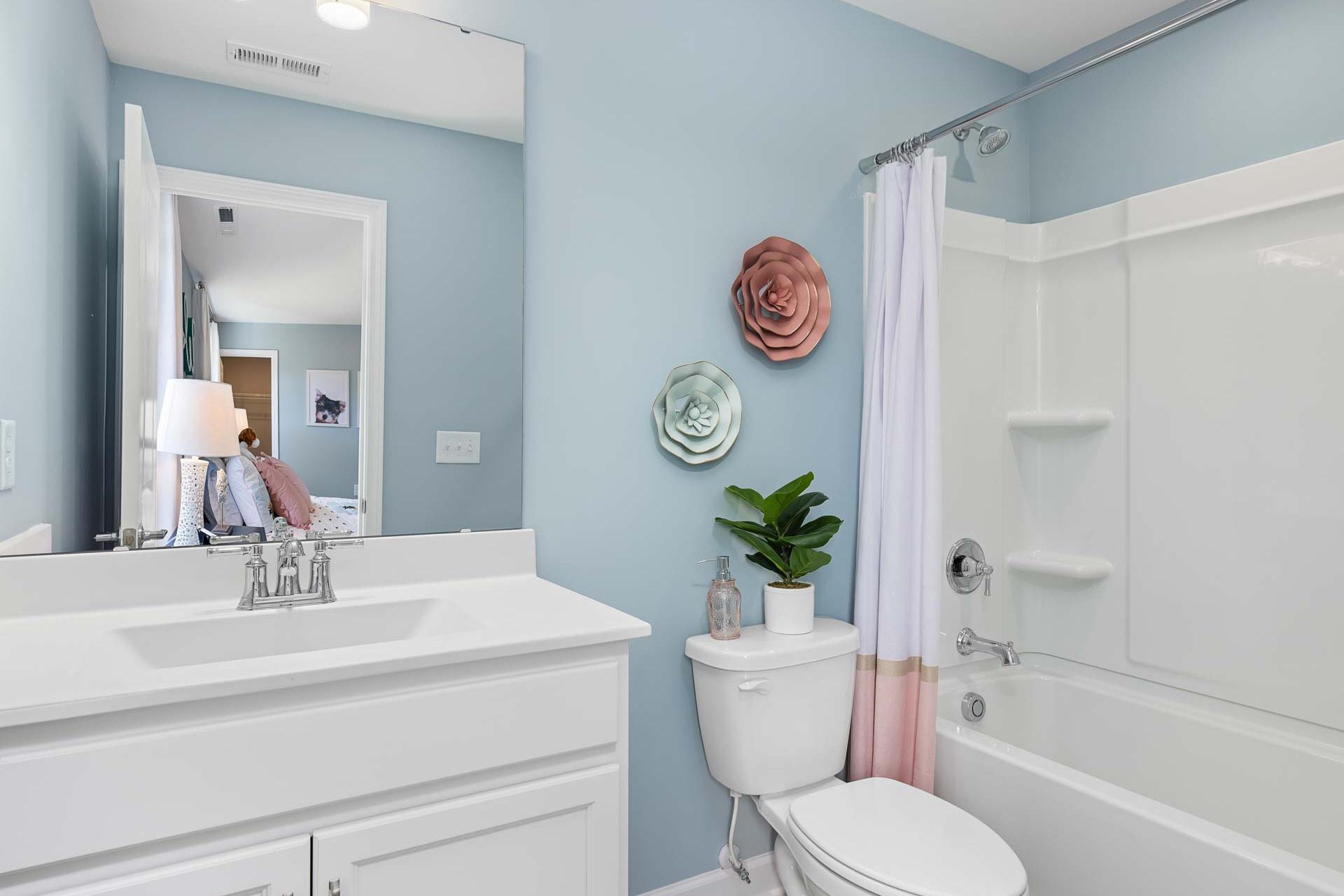 Guest bathroom in Highland Forest Fuquay-Varina NC home with light blue walls, pink floral shower curtain, white vanity sink, and potted plants