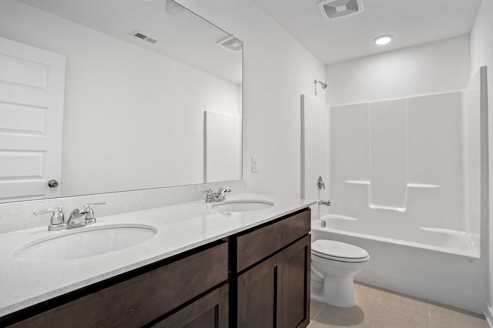 Modern bathroom with double vanity sinks, tub-shower combo, and storage cabinets in Davidson Homes The Logan C, Sage Farms, White House, TN